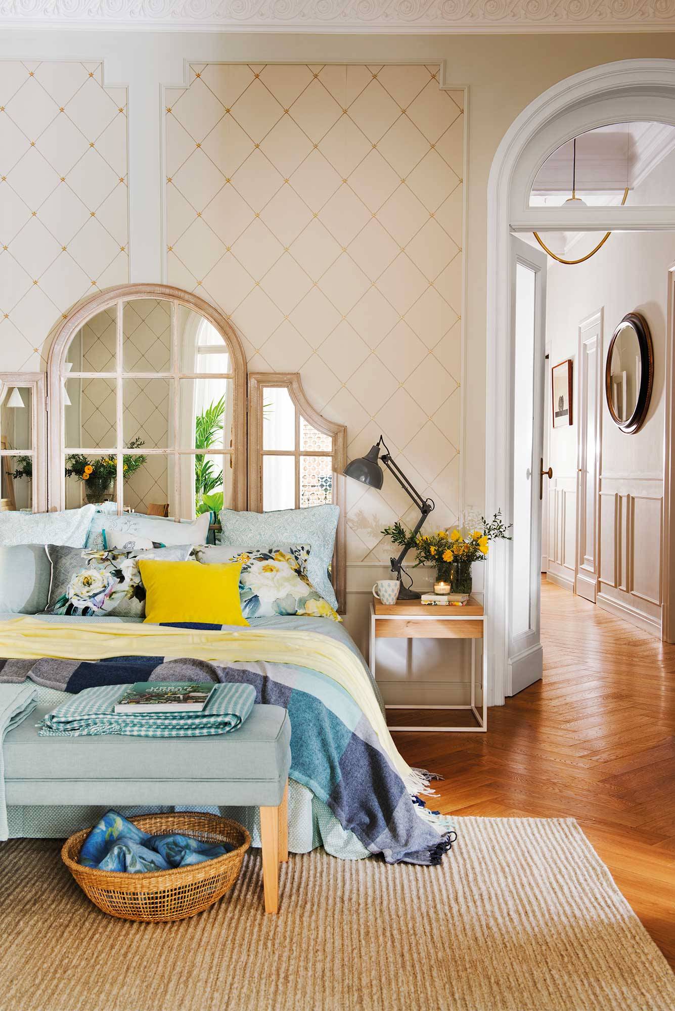 Dormitorio de primavera con espejo tríptico en el cabecero y papel pintado geométrico. 