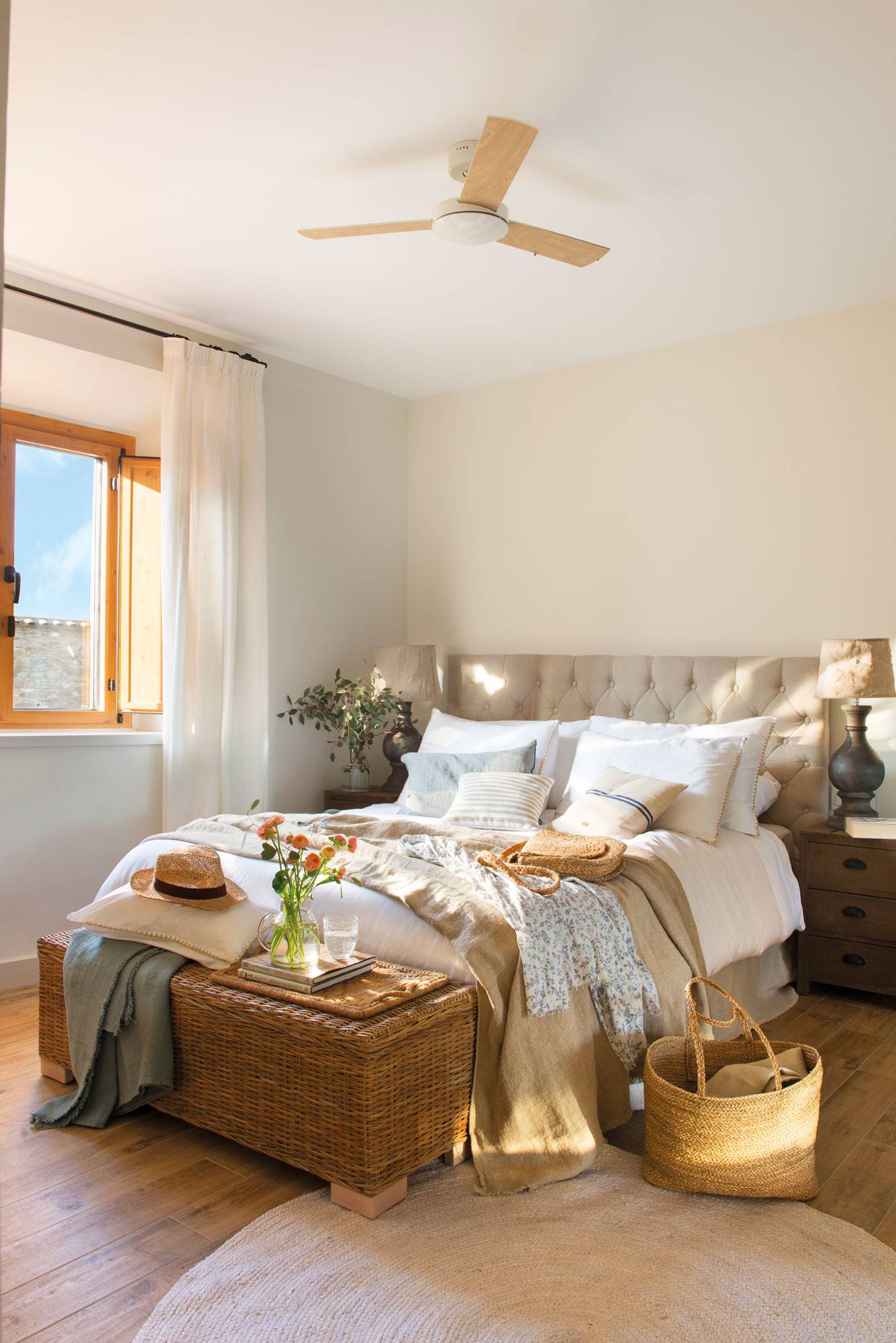Dormitorio de primavera con cabecero gris, baúl de fibra a los pies y ventilador de techo. ventilador de techo