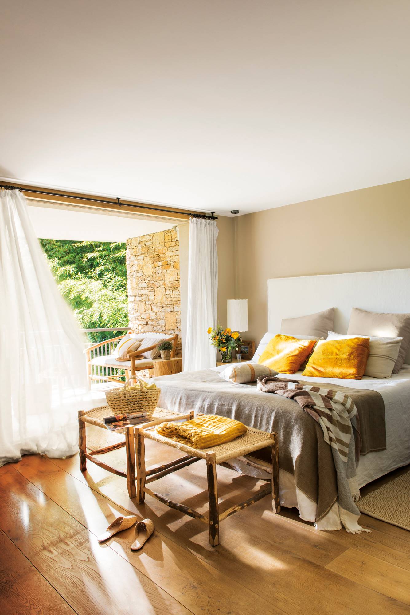 Dormitorio de primavera muy natural con cabecero textil blanco, paredes beiges y banco de fibra y madera.
