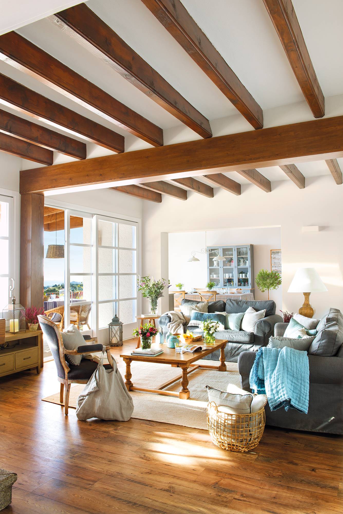Salón con vigas de madera, sofás en azul grisáceo y mesa de madera.