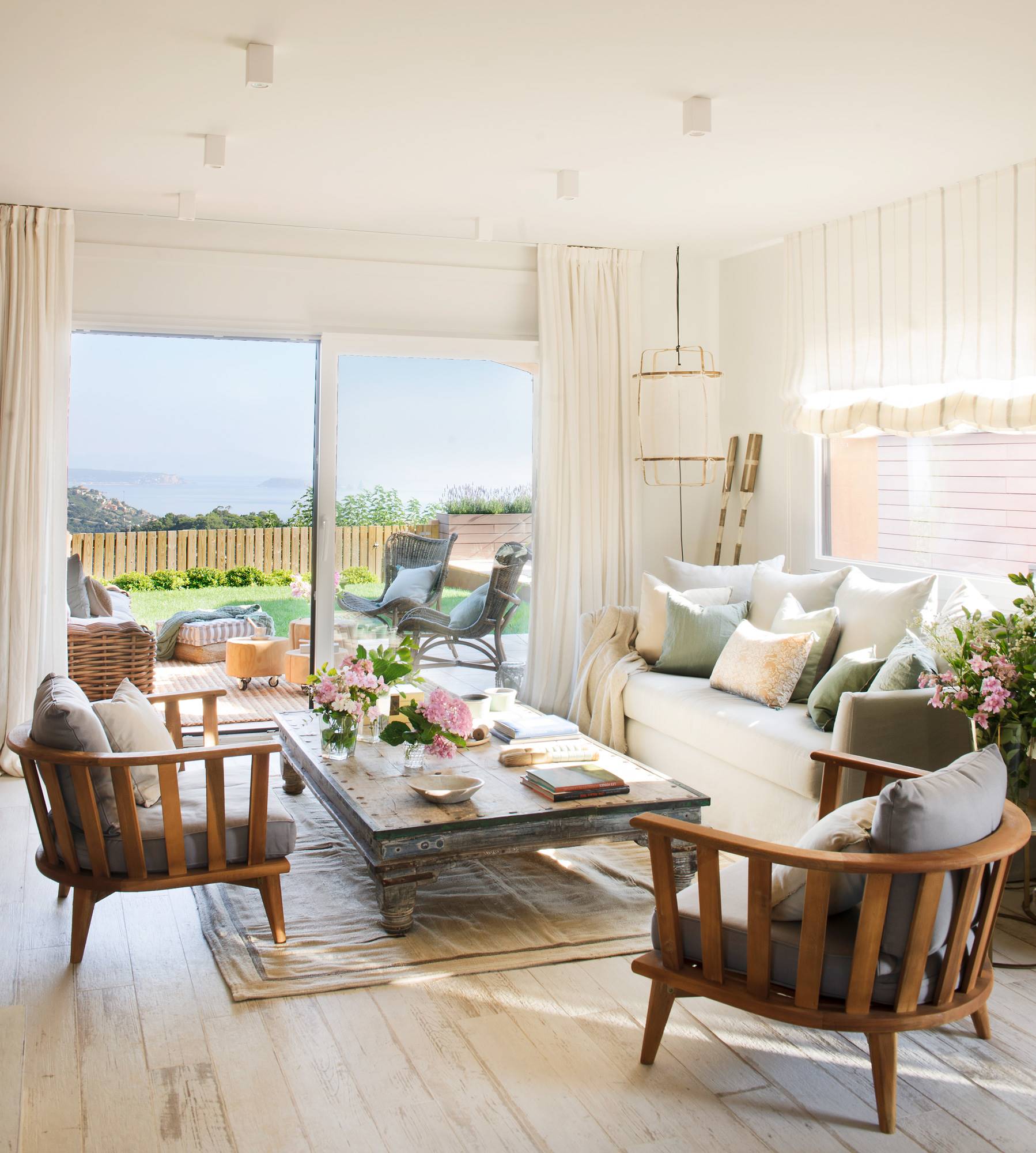 Salón abierto al jardín con sofá blanco y butacas redondas de madera.
