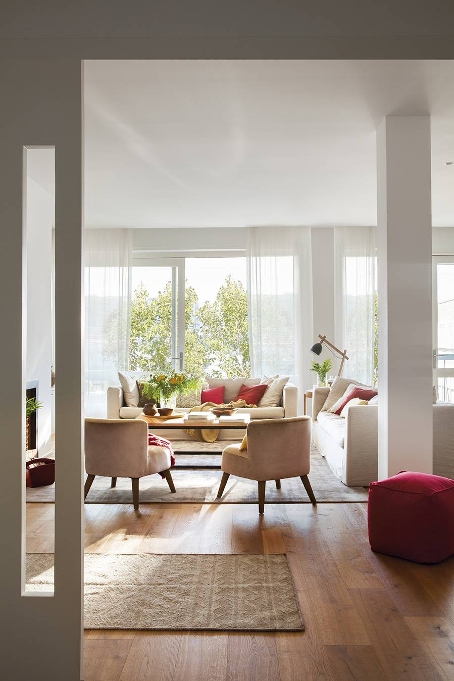 Salón con techos altos con sofá en tonos beige y cojines y puffs en rojo.