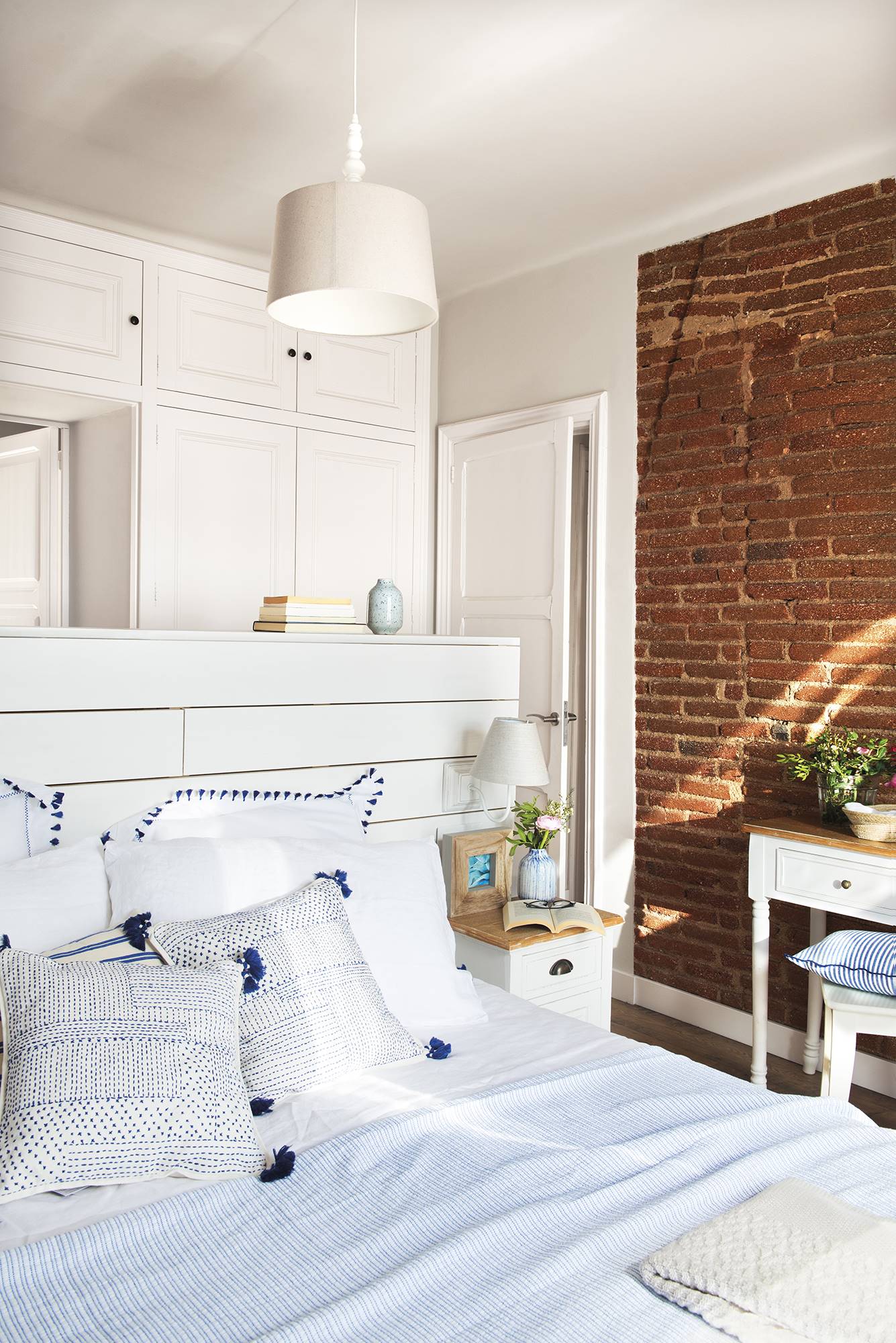 Dormitorio blanco con cabecero de palés y pared de ladrillo vista.