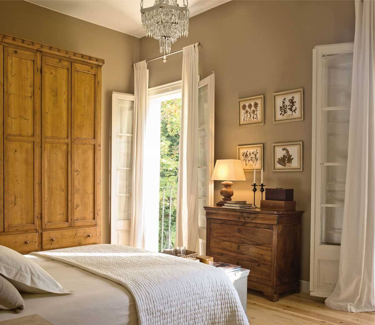 Dormitorio con armario y cómoda de madera, paredes topo, cuadros y lámpara de sobremesa encendida-257408