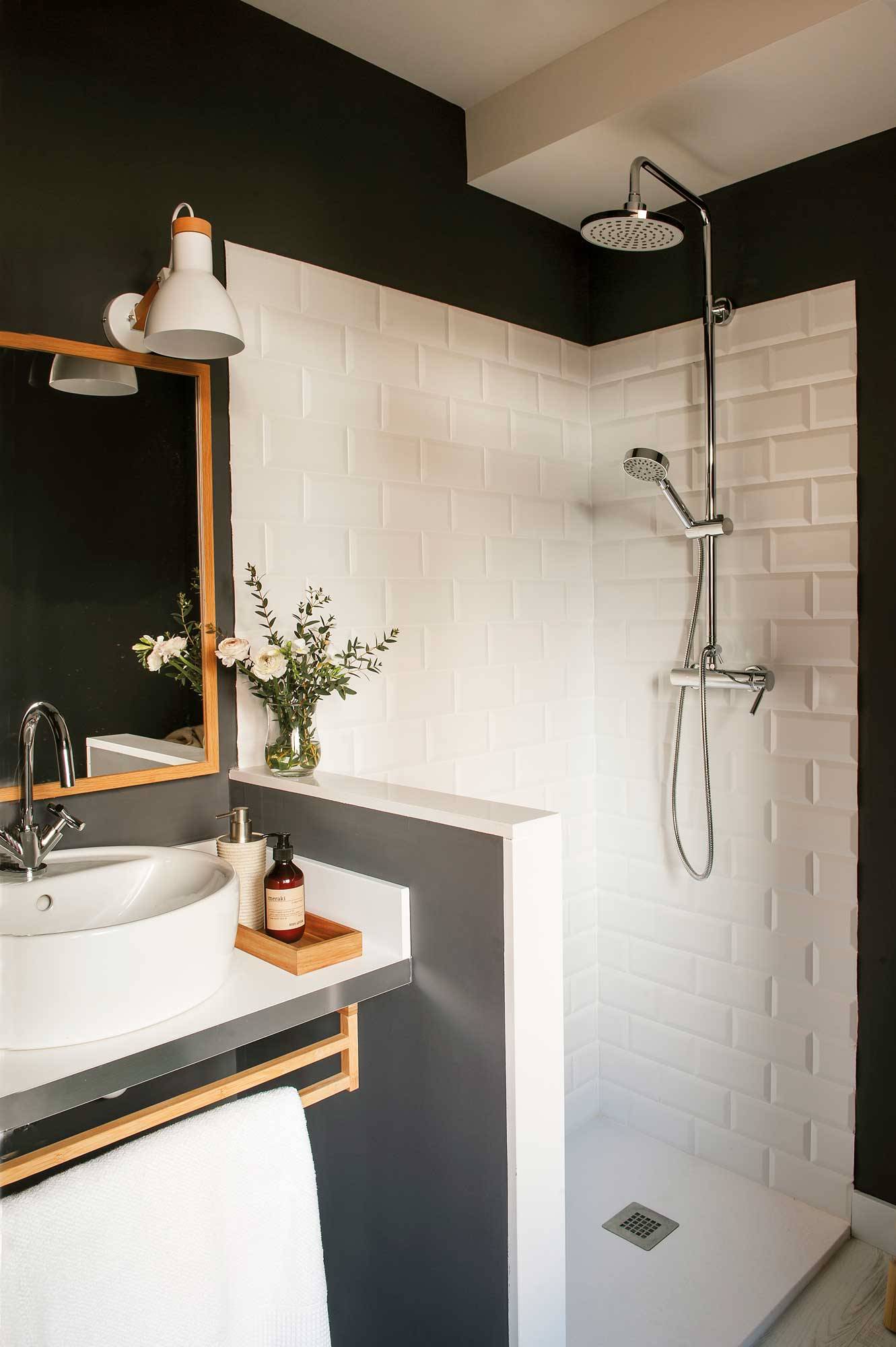 Baño con paredes negras y azulejos blanco tipo metro con un murete que separa la ducha del lavabamanos.  