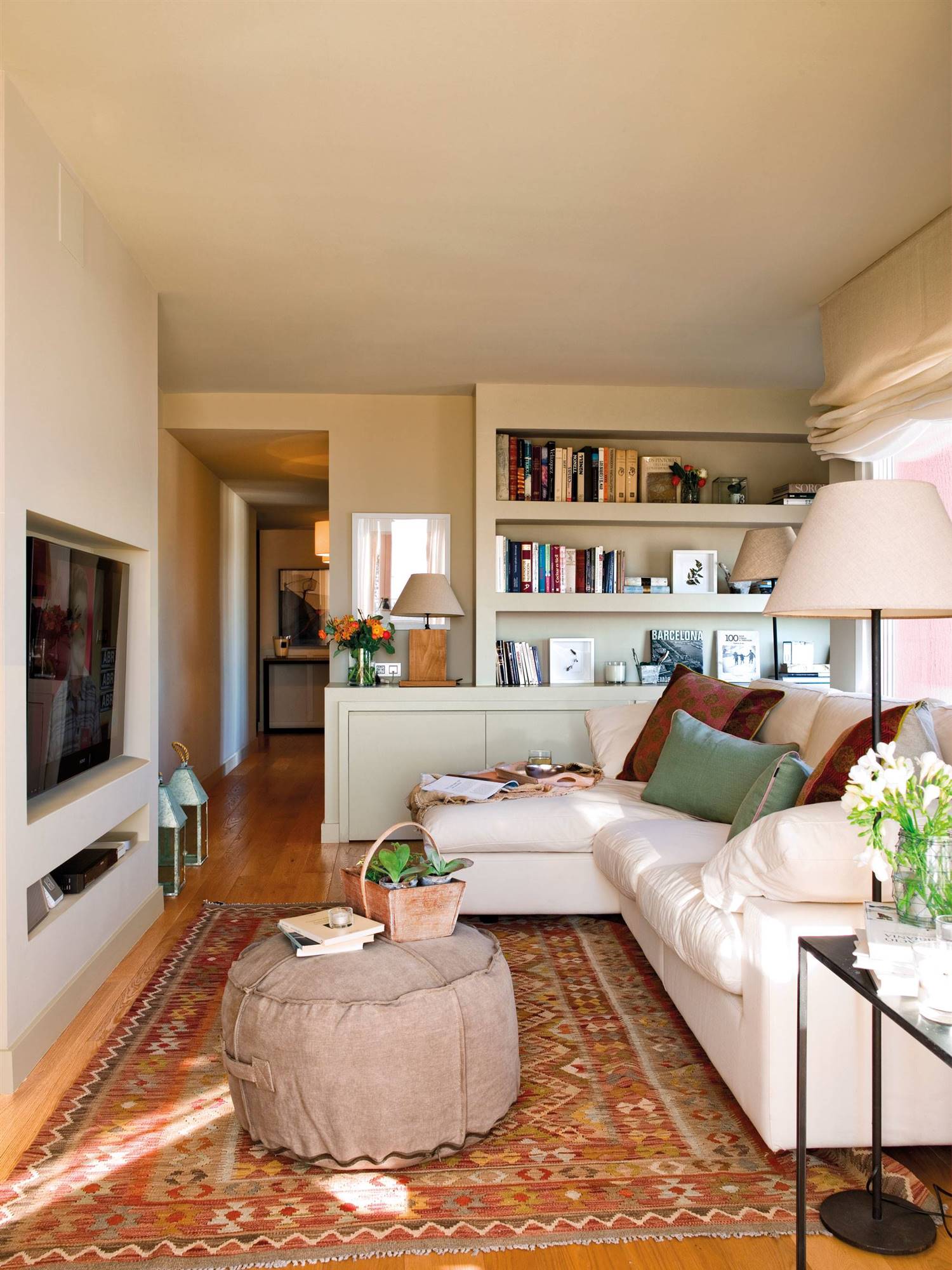 Salón con sofá con chaise longue blanco, alfombra kilim y puff de tela. 