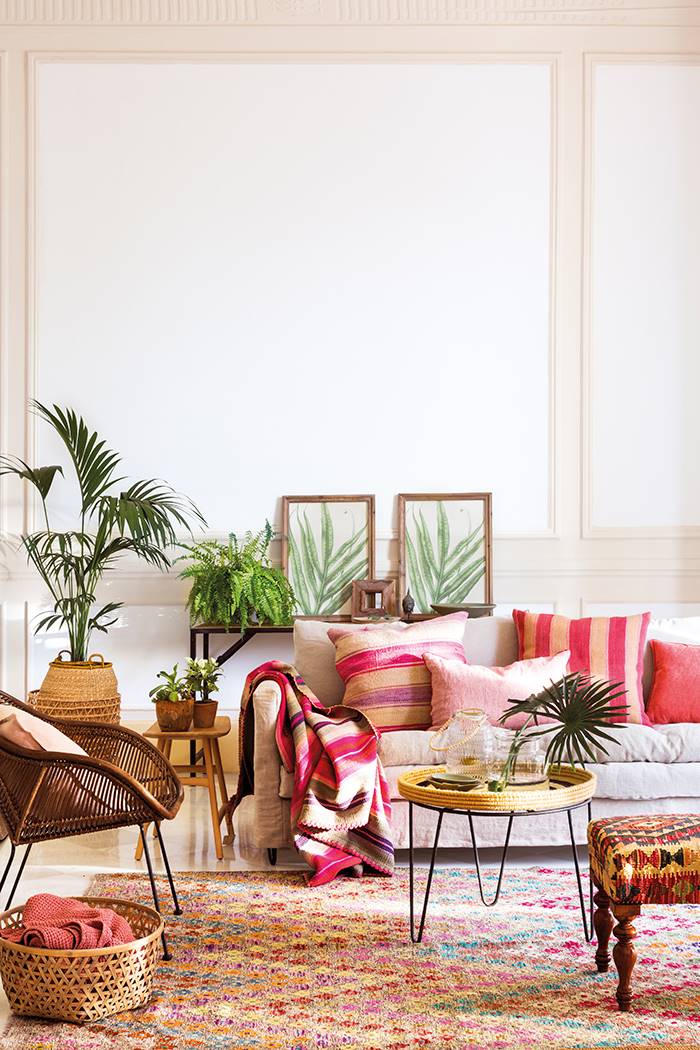 Salón con cojines a rayas en colores rosa y rojo, plantas, cuadros de plantas, alfombra de colores, fibras y estilo de decoración étnico