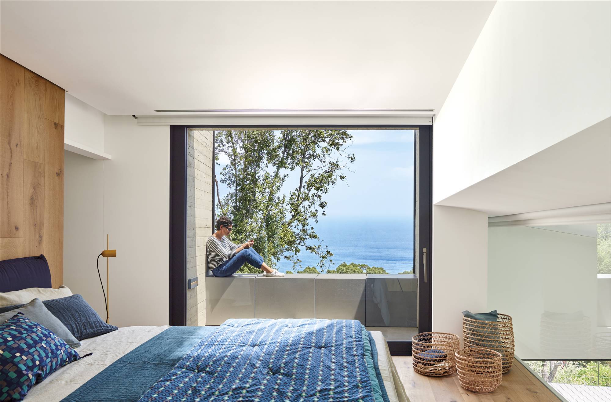 Dormitorio veraniego en tonos azules y blancos con un gran ventanal con vistas al mar
