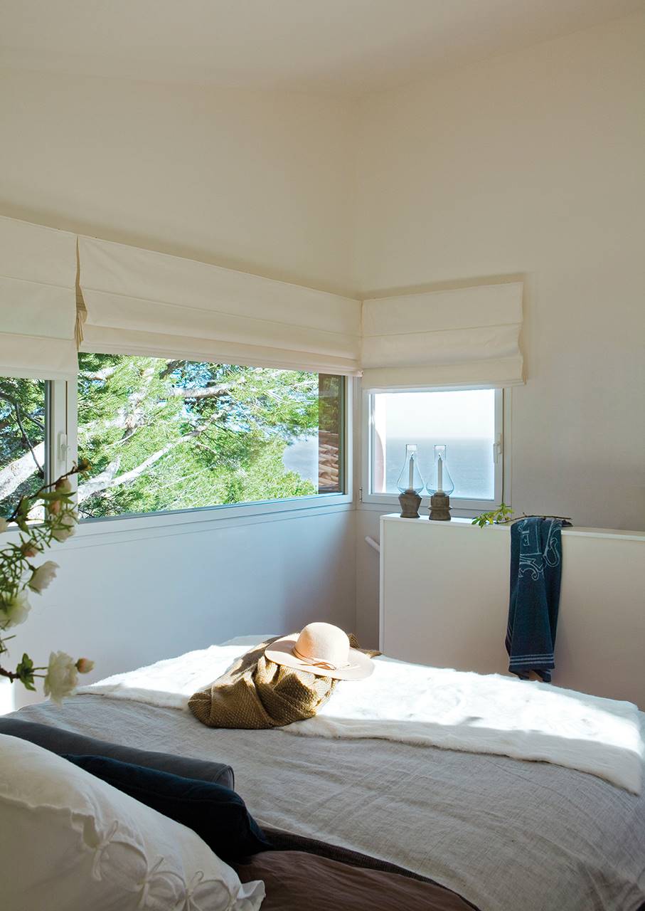 Dormitorio con vistas al mar a través de los grandes ventanales con estores blancos.