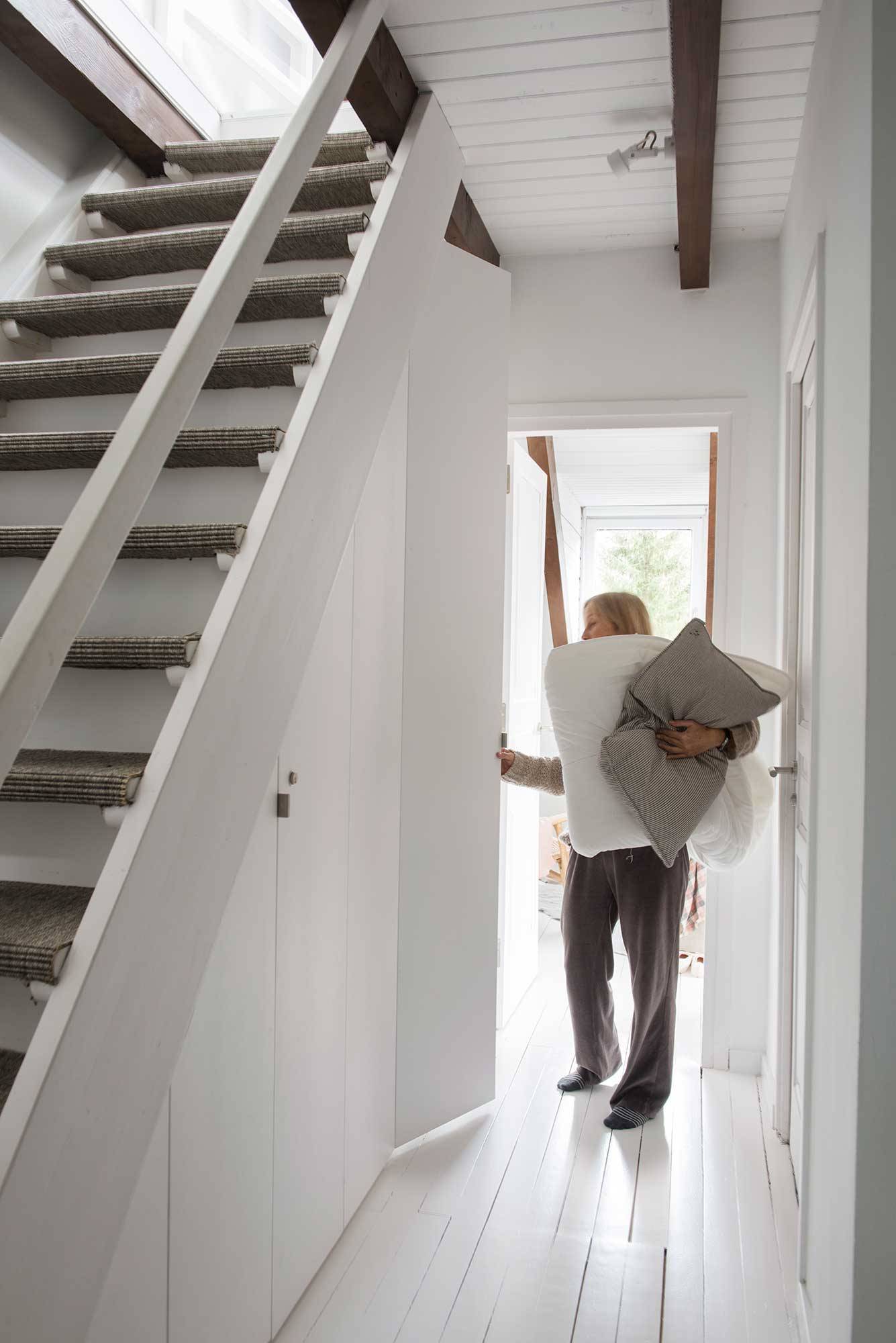 Pasillo de casa alpina blanca con armarios integrados bajo la escalera y mujer con ropa de cama