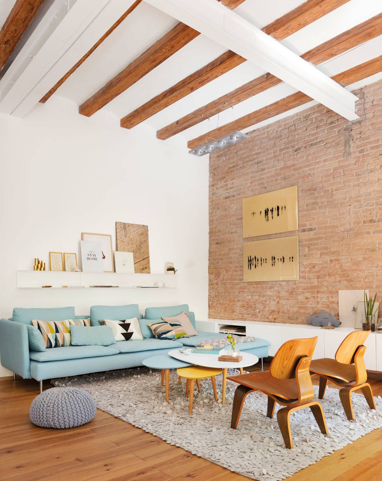 Salón pequeño con vigas de madera, pared de ladrillos vistos y sofá en verde azulado suave