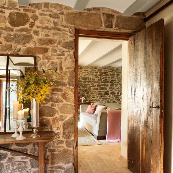 Recibidor rústico con pared de piedra, puerta de madera, consola de madera, espejo, velas y mimosas-360215