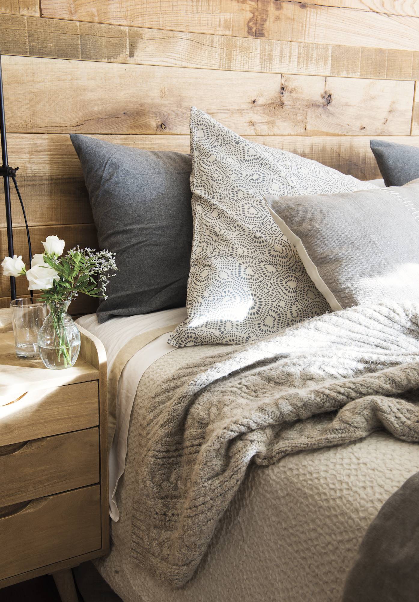 Detalle dormitorio con cabezal de madera y ropa franela gris.