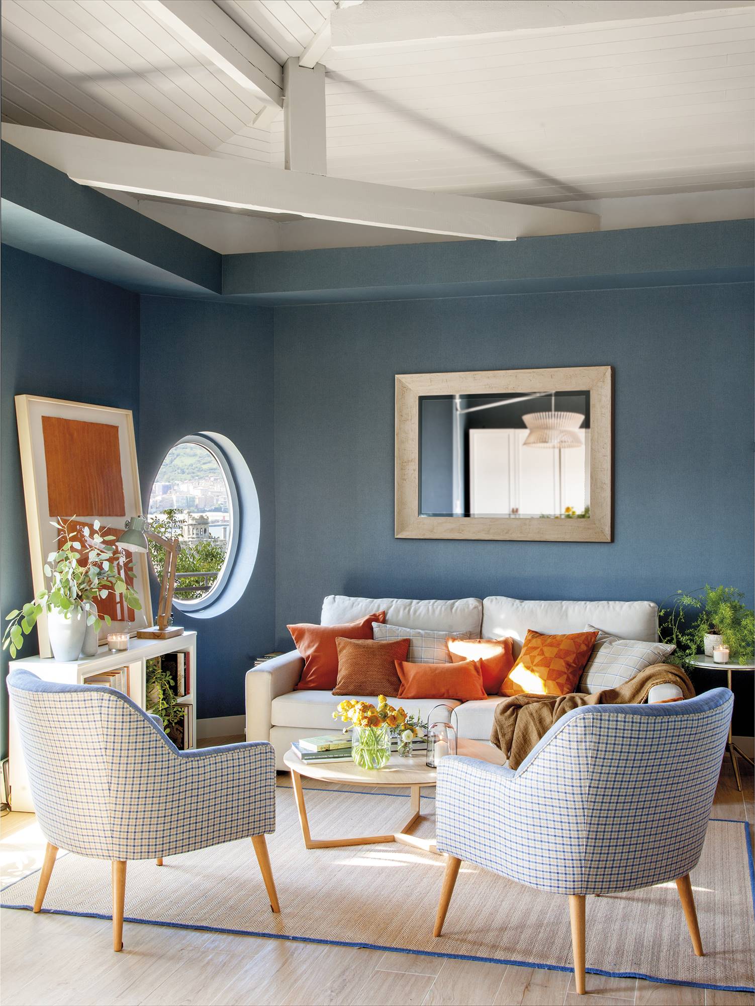 Salón con paredes azules, sofá blanco y textiles en naranja. 