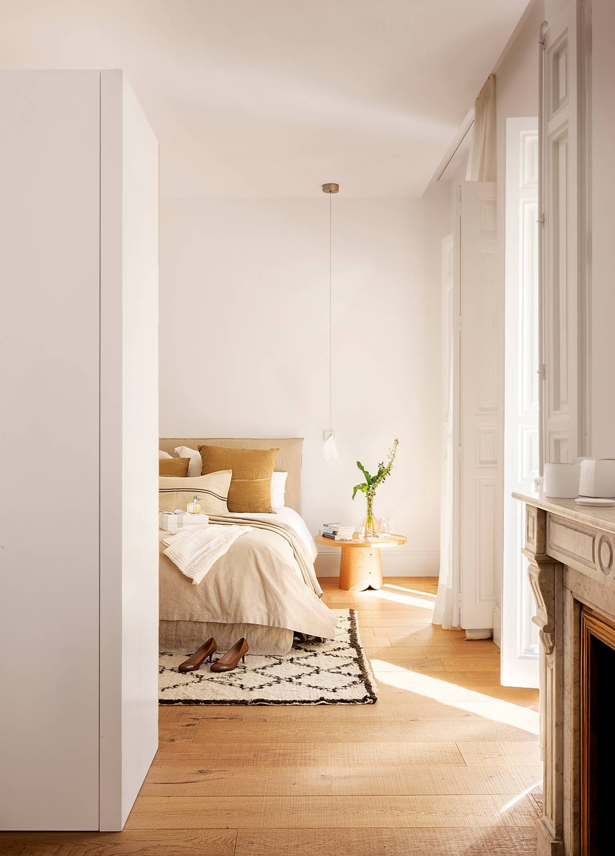 Dormitorio con suelos de madera, alfombra bereber y ropa de cama beige. 