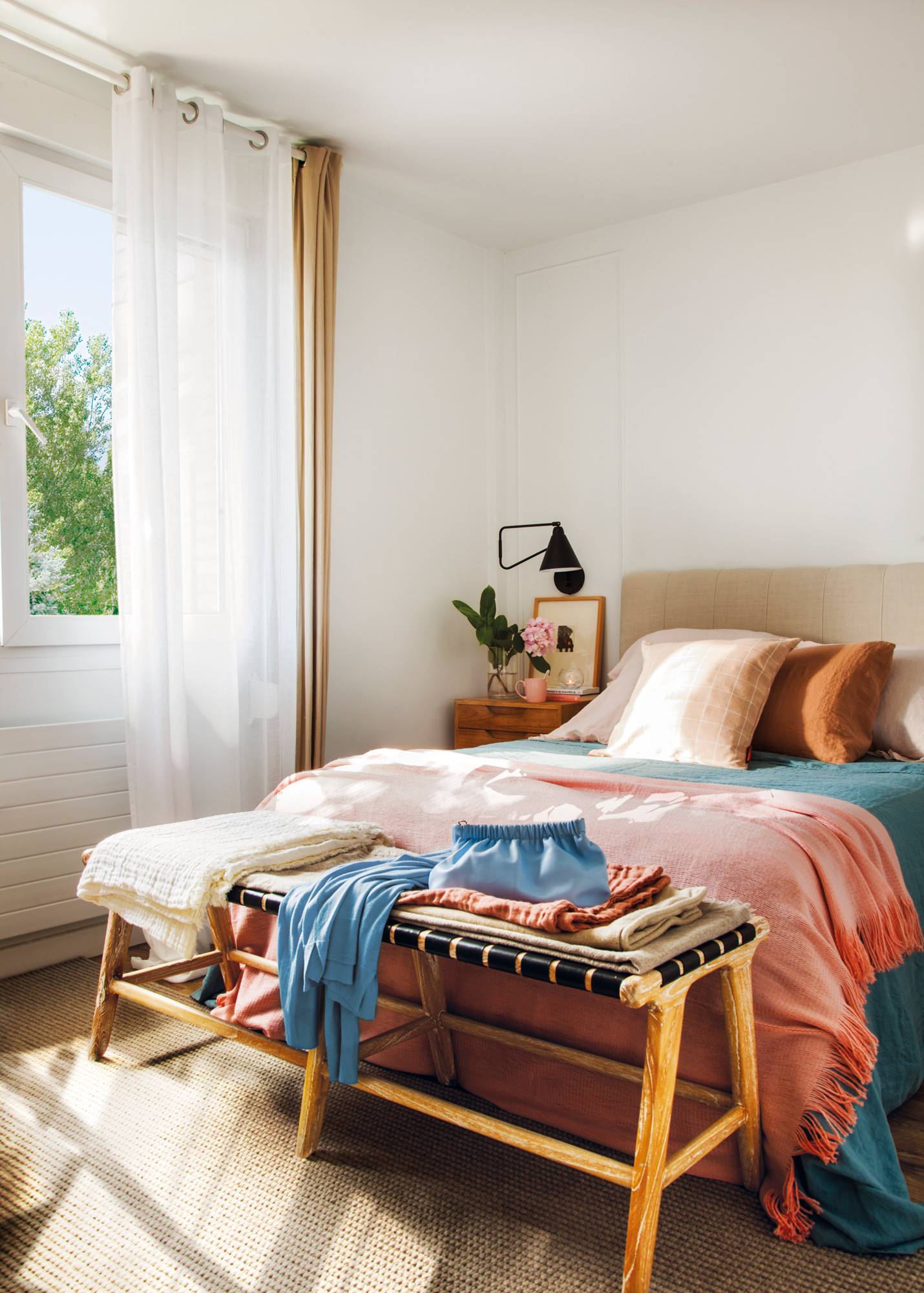 Dormitorio con cabecero de lino y banco a pie de cama. 