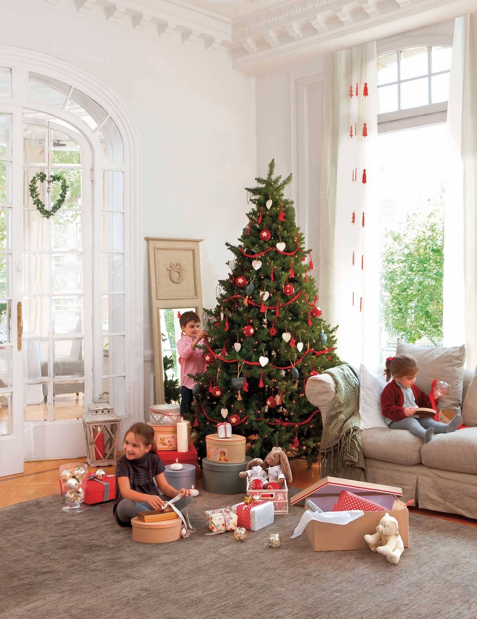 Salón decorado en tonos crudos con sofá gris, puertas de cristal y árbol de Navidad decorado con guirnaldas y adornos rojos. 