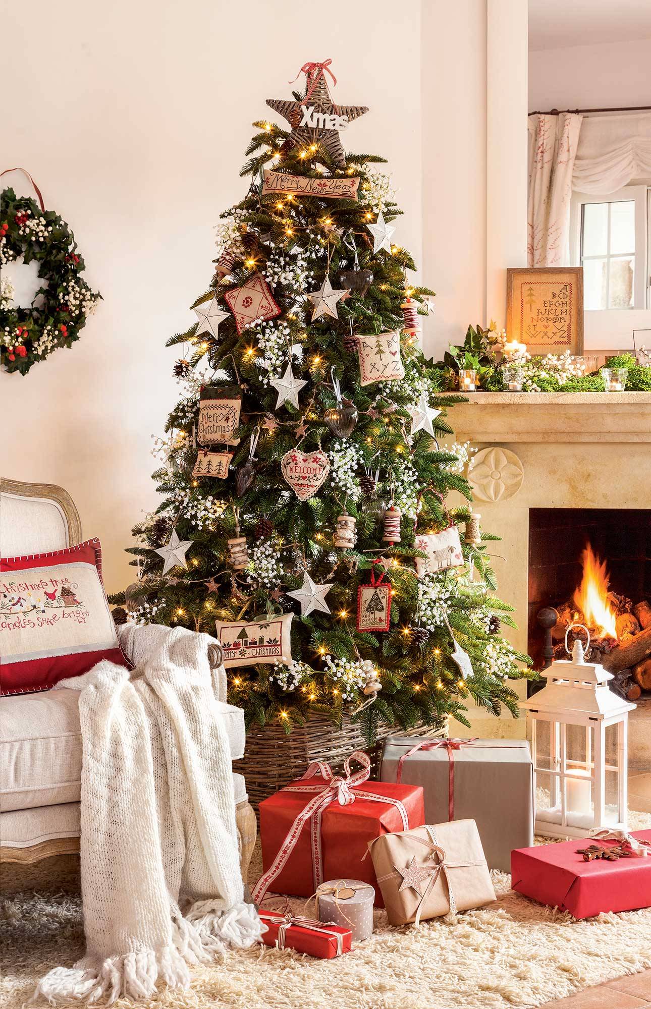Salón con árbol de Navidad junto a la chimenea con adornos navideños bordados a punto de cruz.  