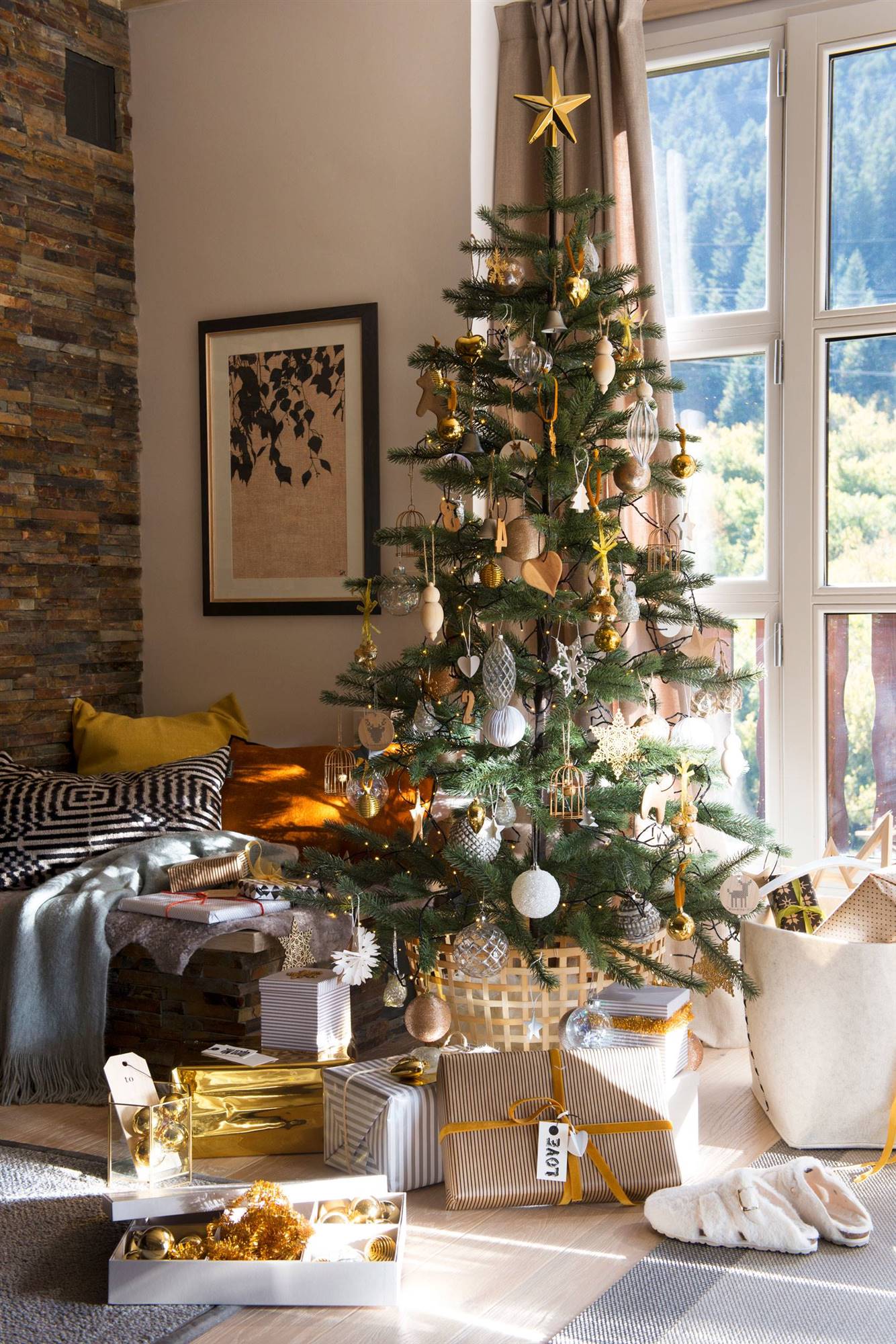 Salón con árbol de Navidad pequeño con decoración dorada y regalos en el suelo.