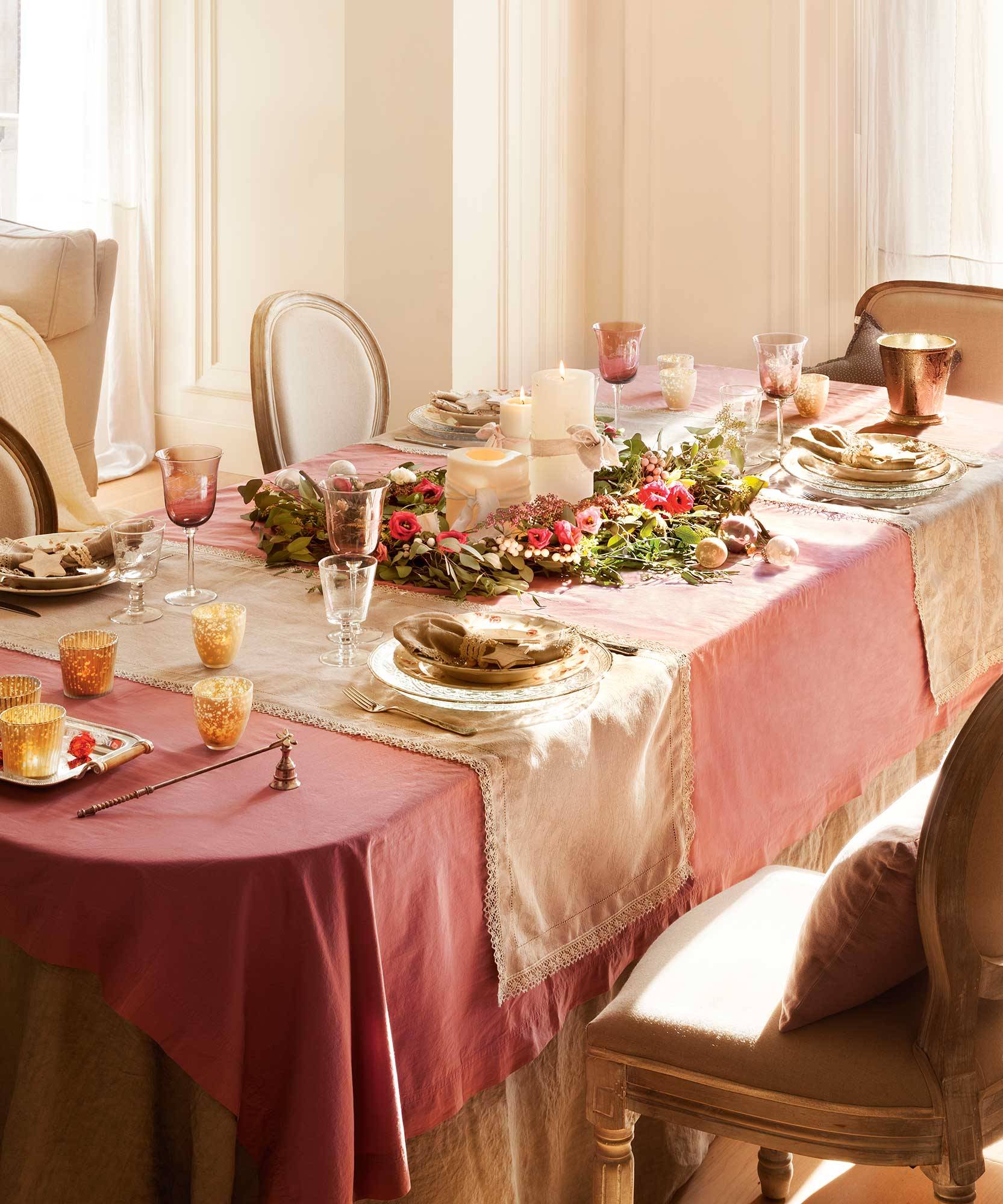 Mesa de Navidad con mantel rosa y caminos de mesa beige. 