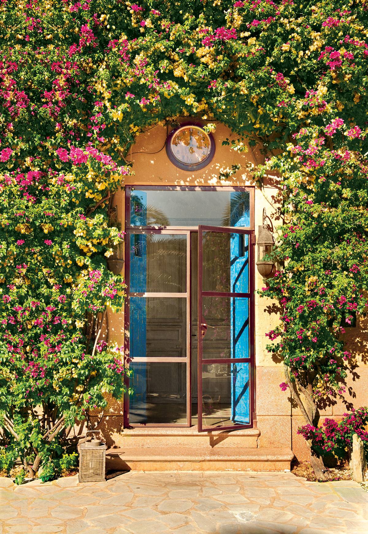 Puerta de entrada a casa rústica con puerta acristalada, reloj y bouganvilla-378425