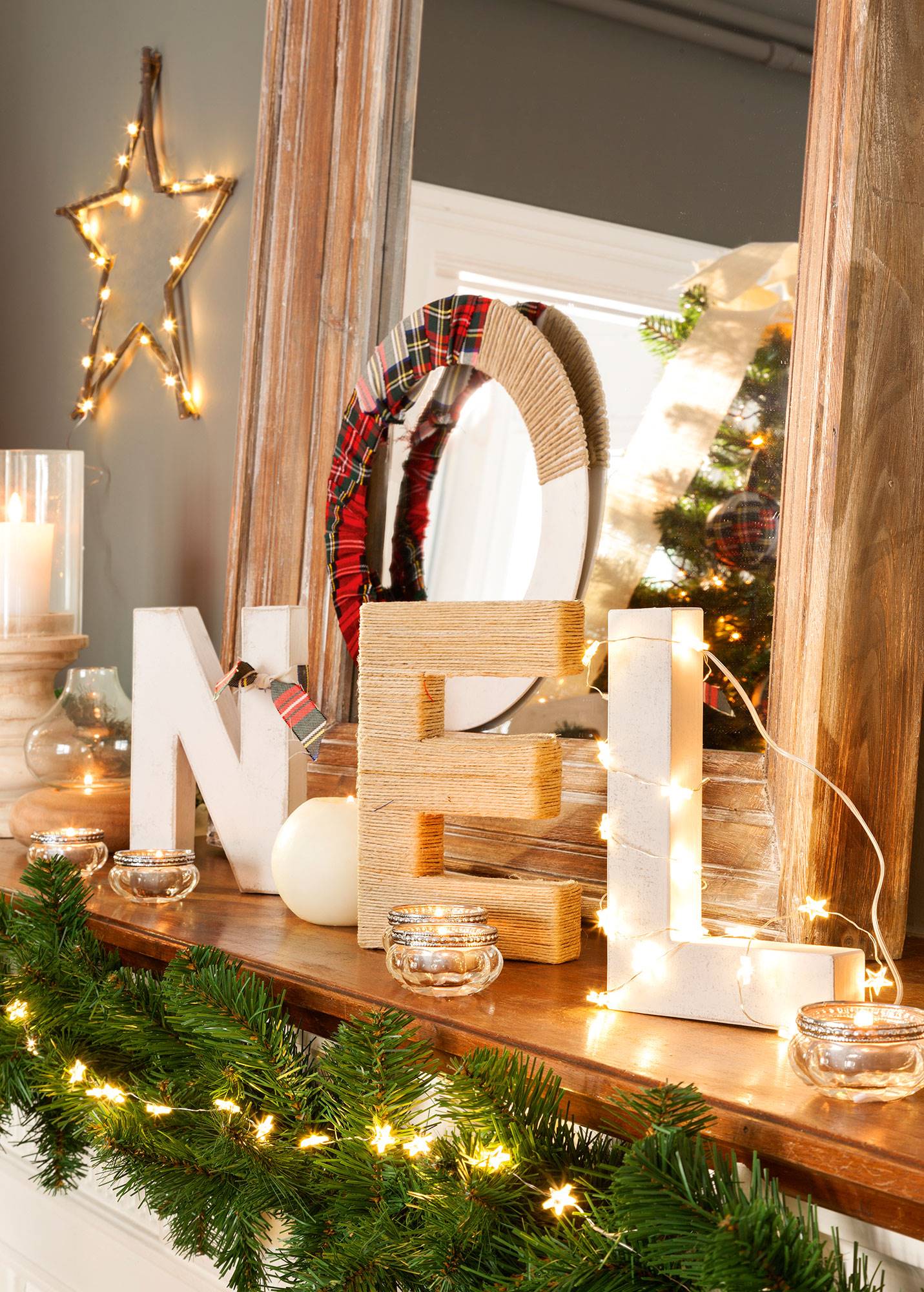 Detalle de repisa de chimenea decorada con la palabra Noel, guirnalda luminosa y velas.