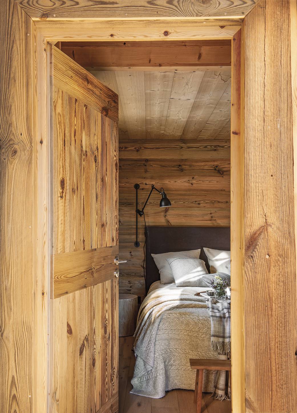 Dormitorio revestido en madera con cabecero de lino y apliques negros. 