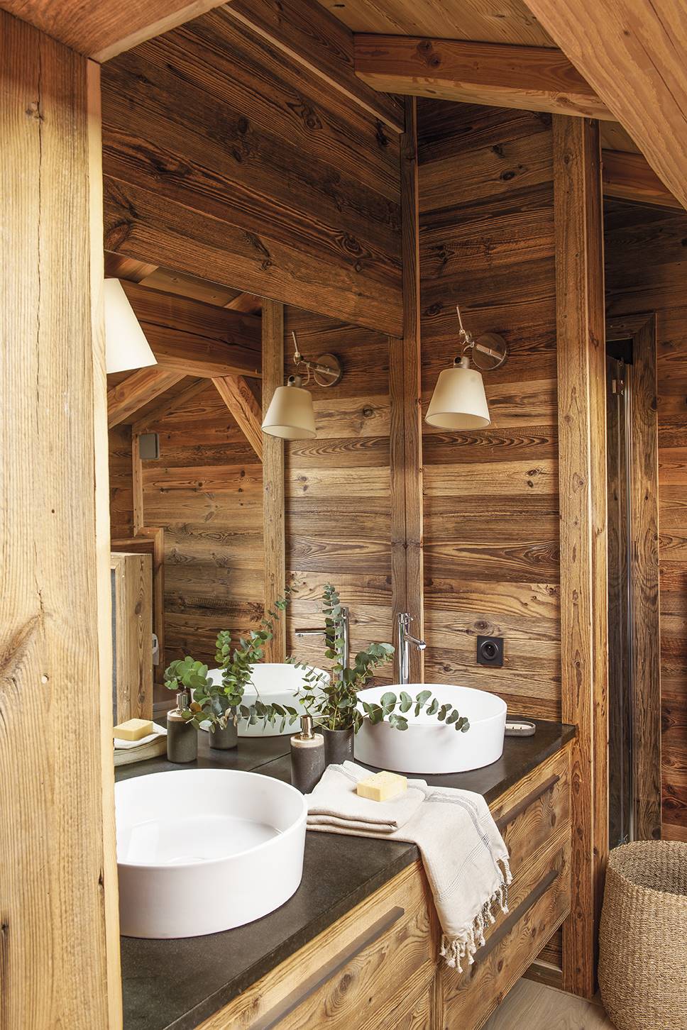 Baño rústico con paredes de madera y lavamos sobre encimera.  