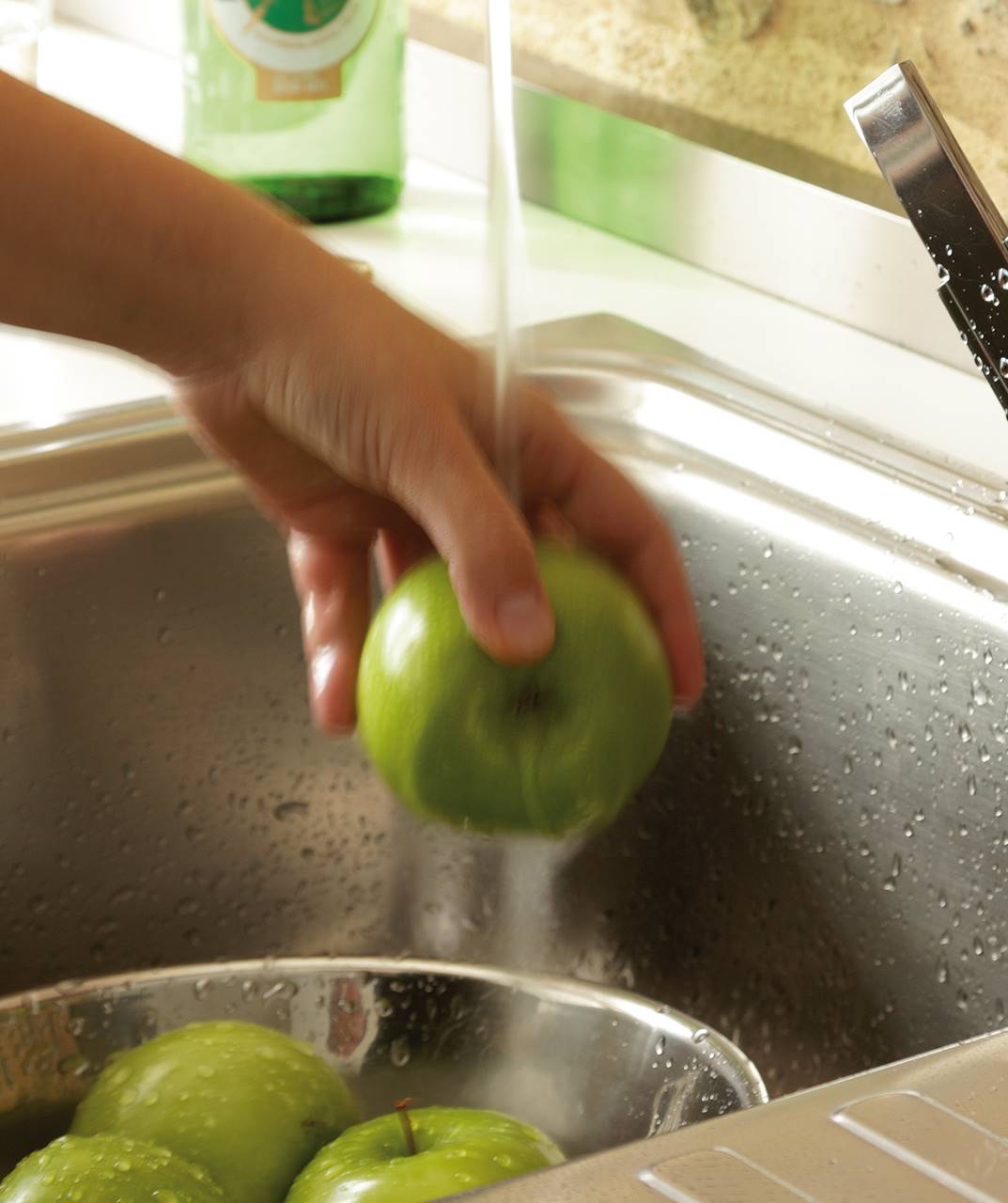Detalle de mano lavando manzanas bajo chorro grifo