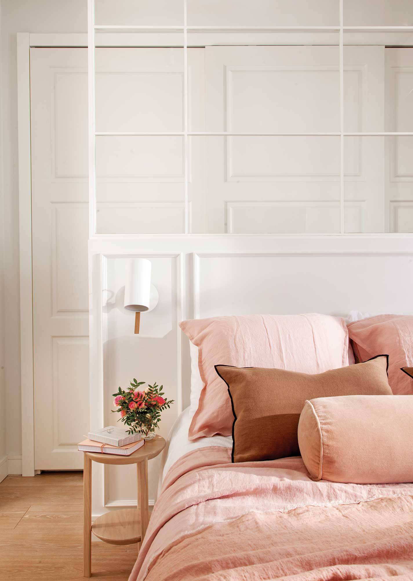 Dormitorio con cabecero acristalado y ropa de cama en rosa.
