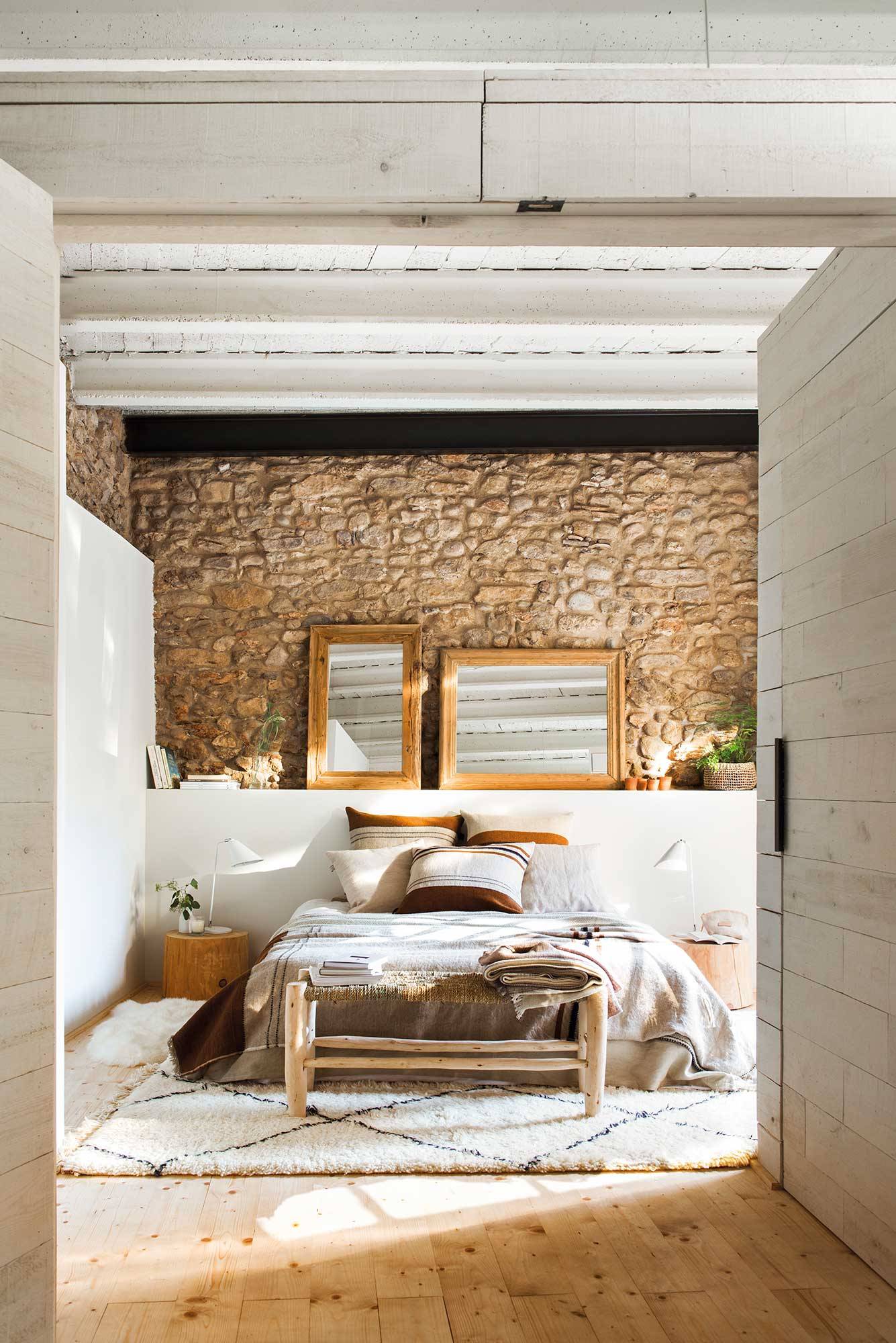 Dormitorio con pared de piedra y cabecero de obra.