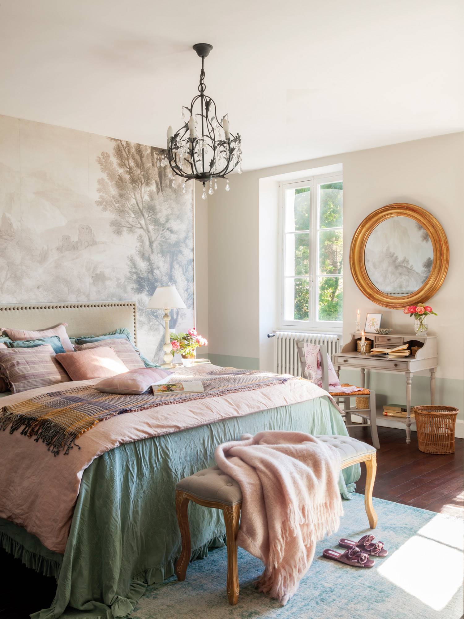 Dormitorio romántico con cabecero tapizado con tachuelas, pared con mural bucólico y lámpara de araña suspendida.