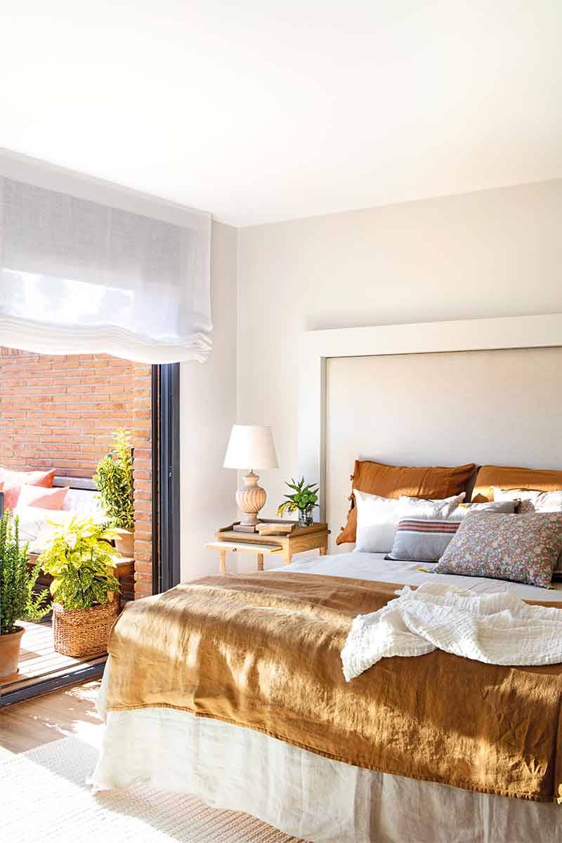 Dormitorio con gran cabecero tapizado enmarcado con listones de madera blanca.