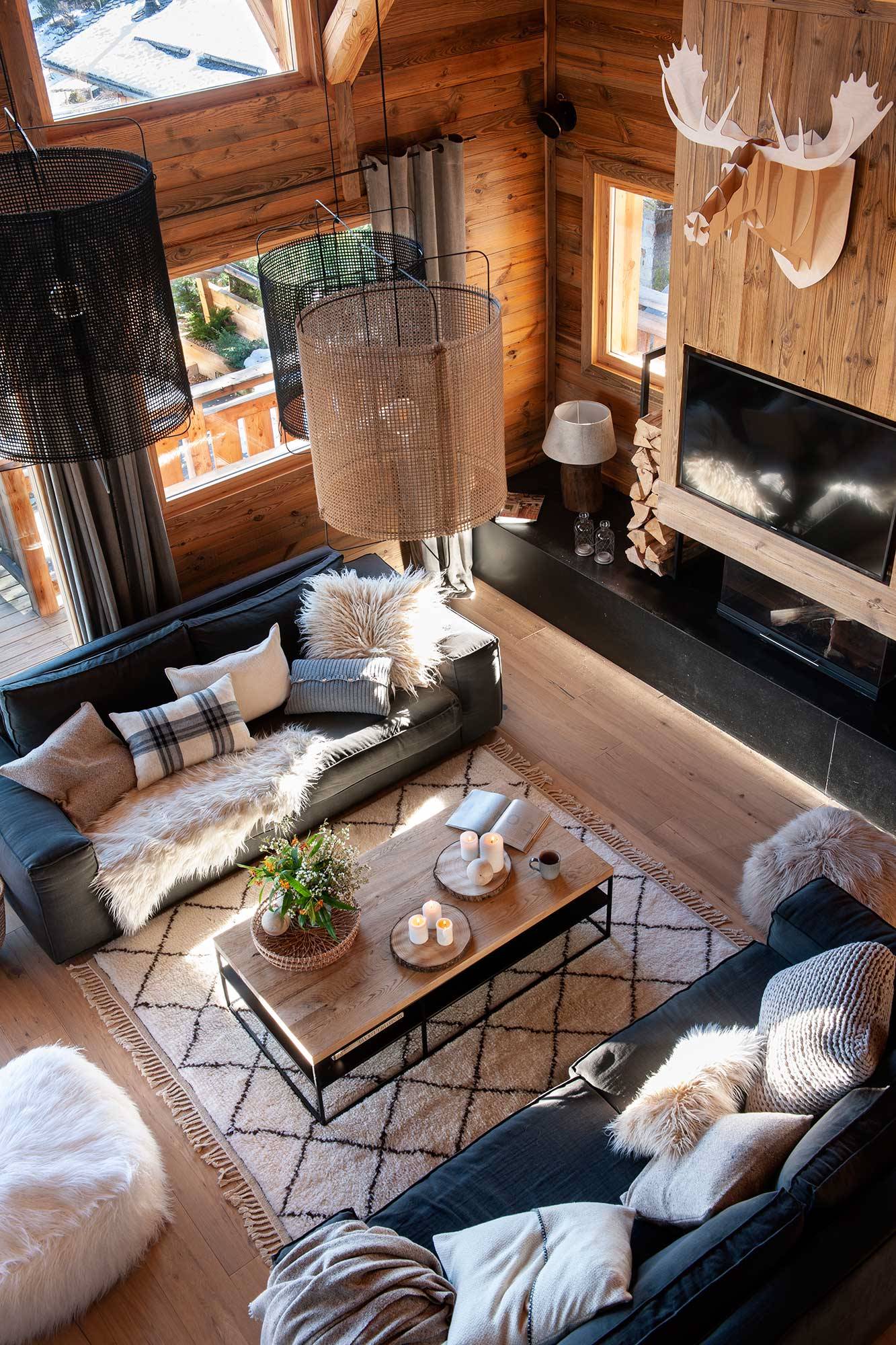 Vista cenital de salón de cabaña de madera con sofás grises y alfombra bereber.