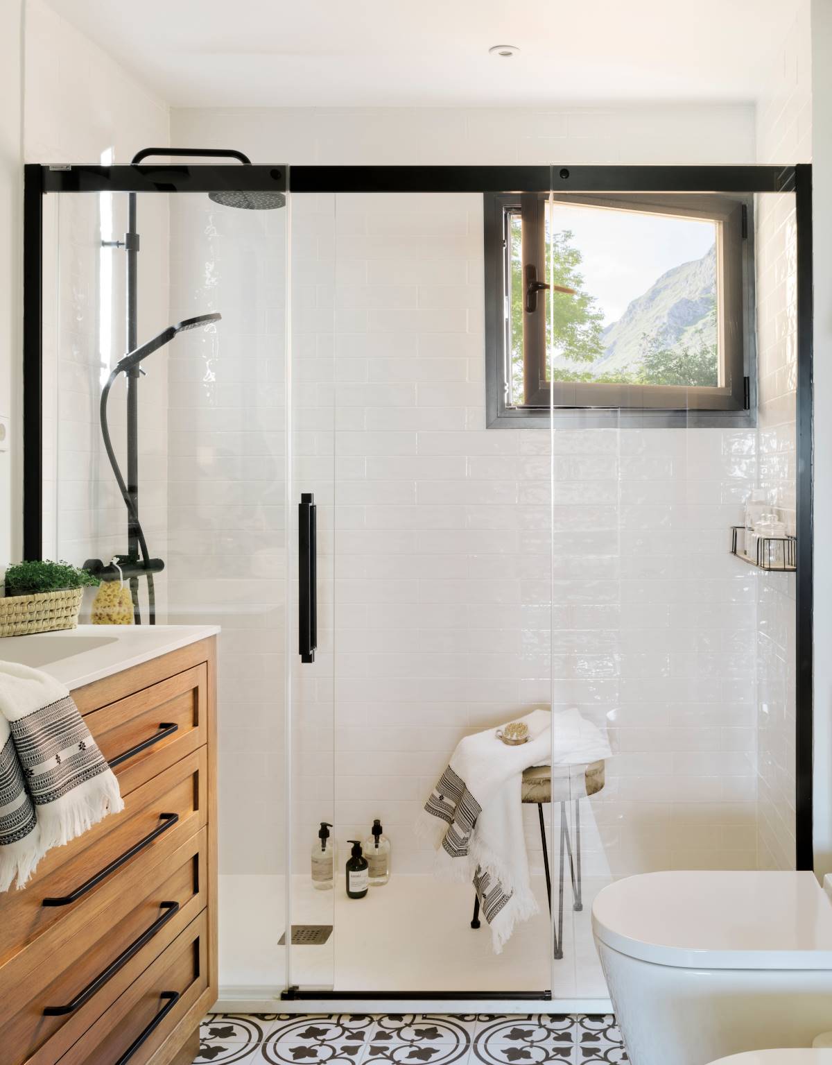 Baño con mampara con perfil negro, mueble de madera y suelo hidráulico.
