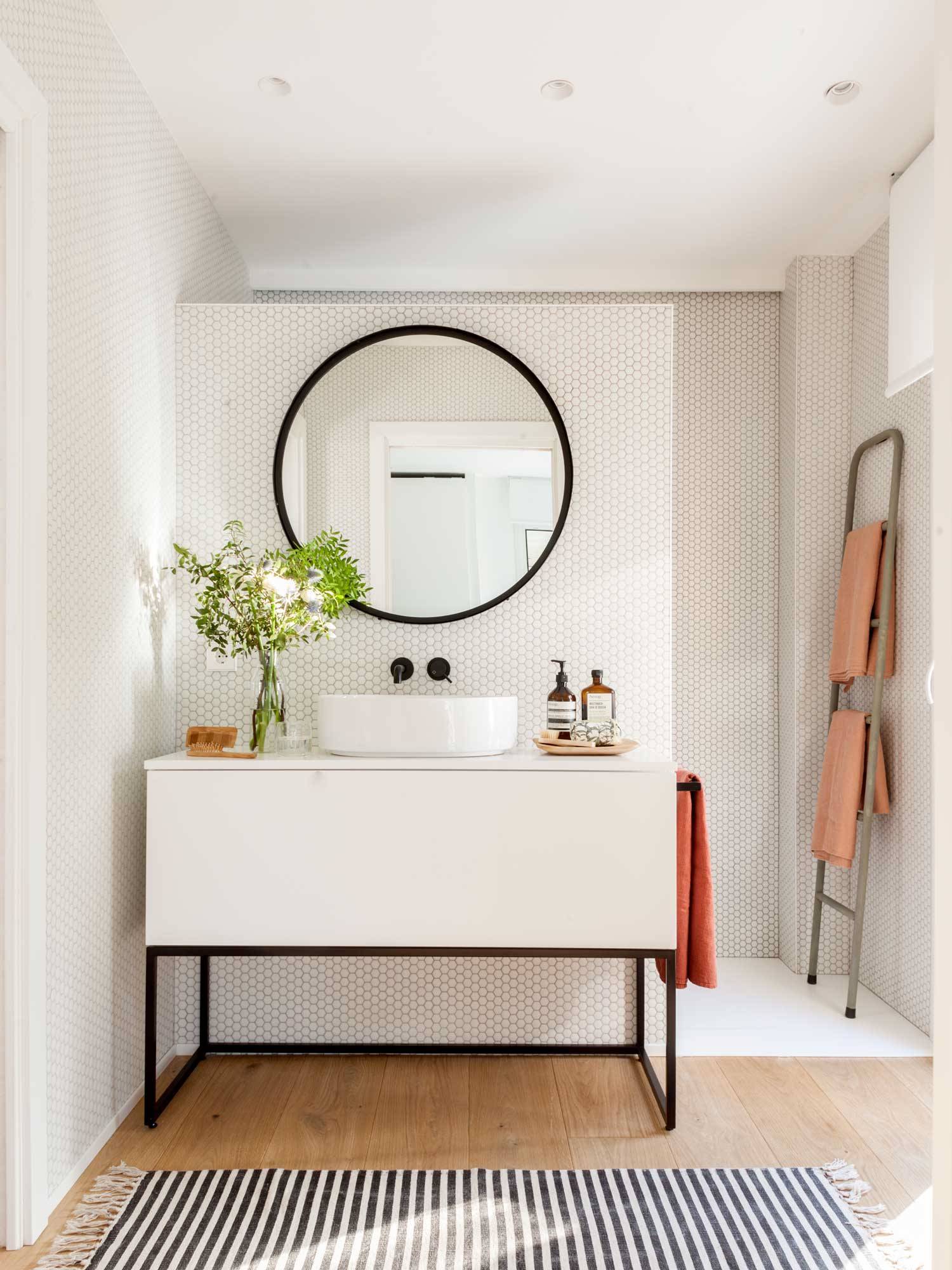 Baño con mueble blanco, pared de mosaico y espejo redondo.