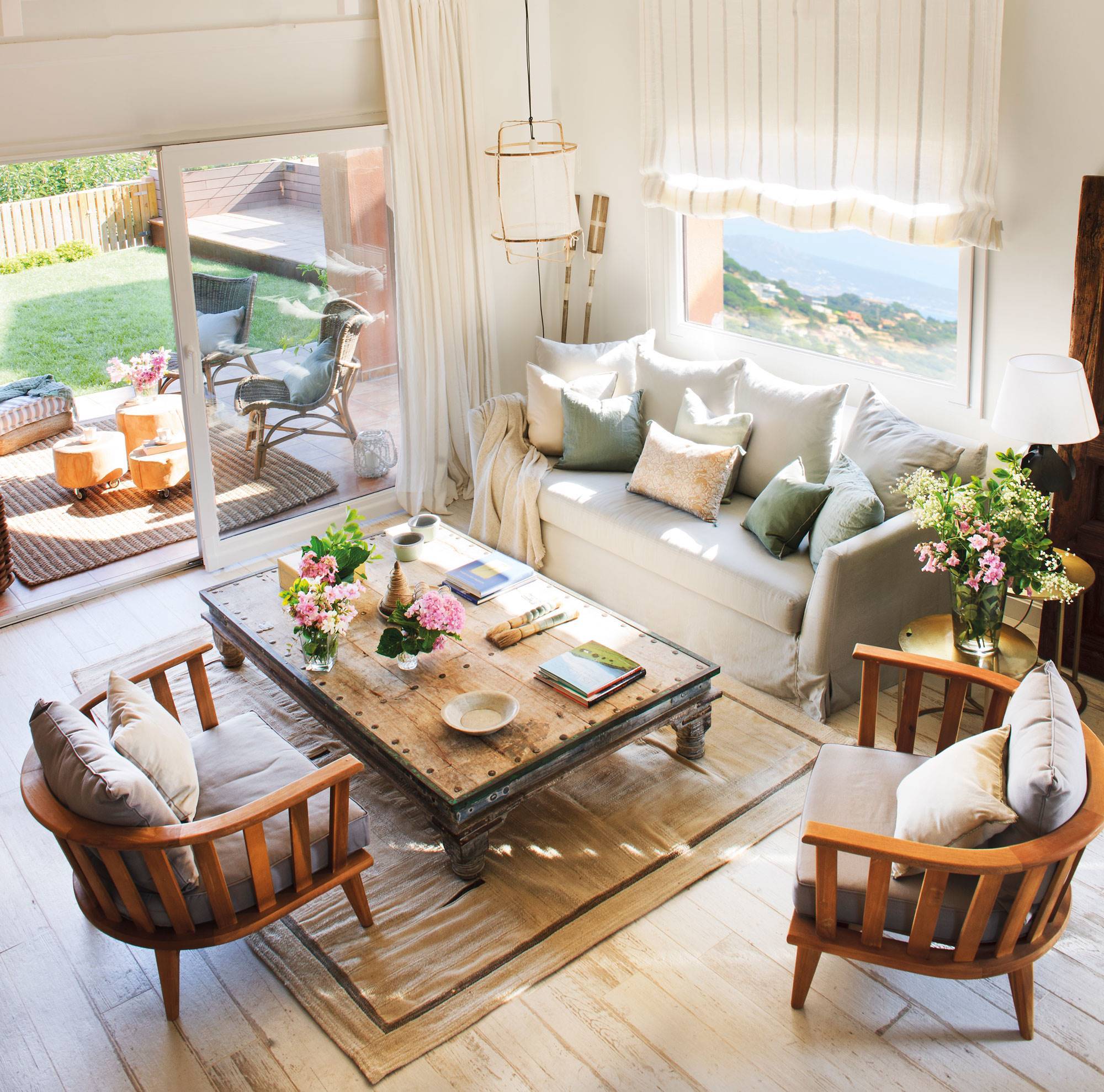 Salón pequeño con gran ventanal al jardín, sofá gris, mesa de centro de madera y butacas grises. 