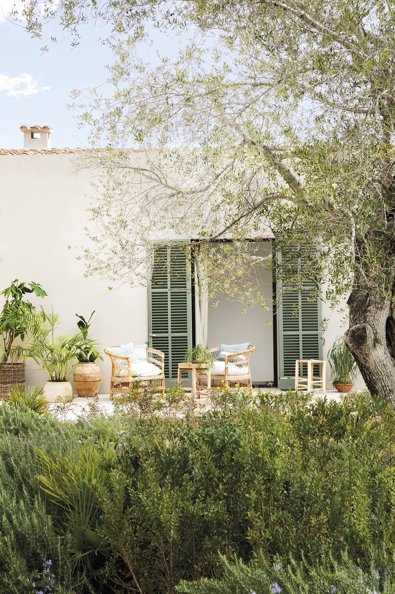 Casa con fachada blanca, puertas verdes y porche con muebles de fibras.