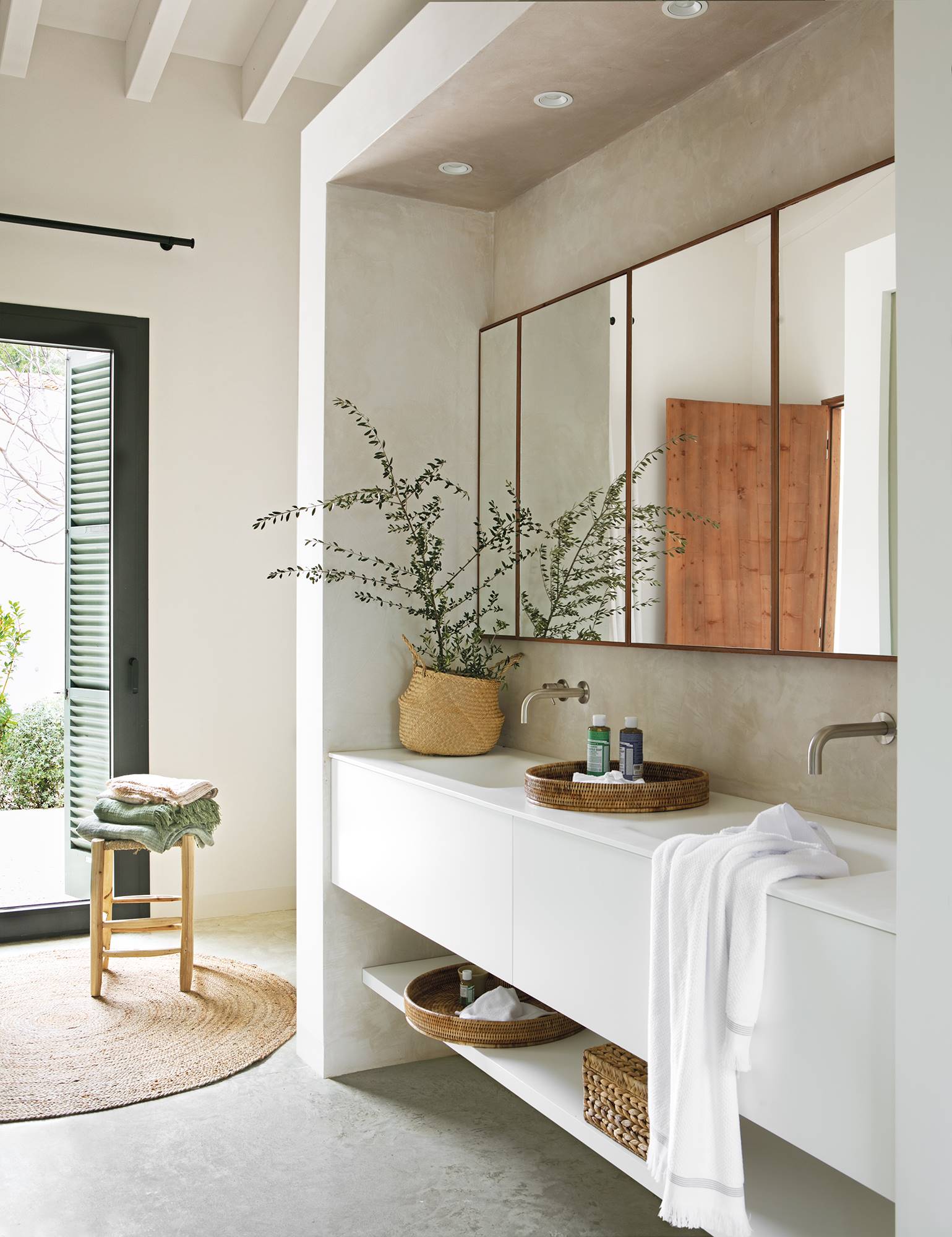 Baño con mueble blanco con balda, espejo, planta y alfombra de fibras.