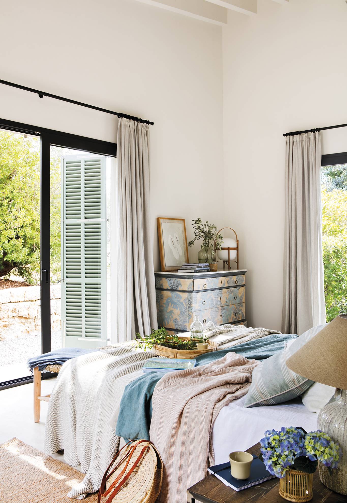 Dormitorio con cama, textiles ligeros, ventanales y cómoda. 