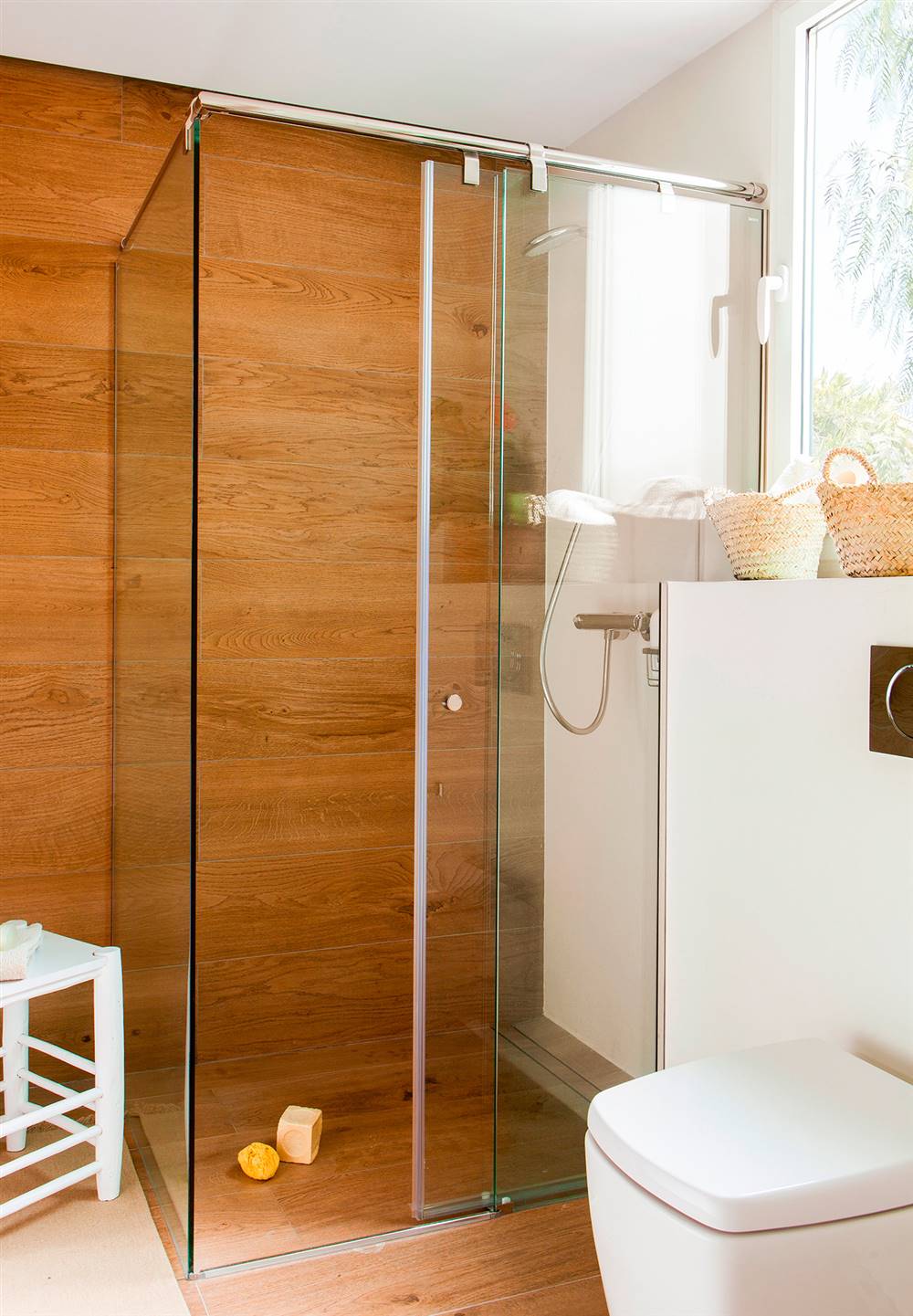 Baño con ducha con mampara corredera de cristal y con suelo y pared revestidas con porcelánico que imita la madera
