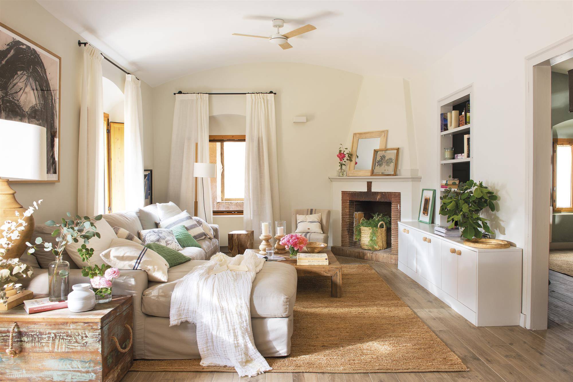 Salón con sofá beige con puff, chimenea, alfombra de fibras y aparador blanco. 