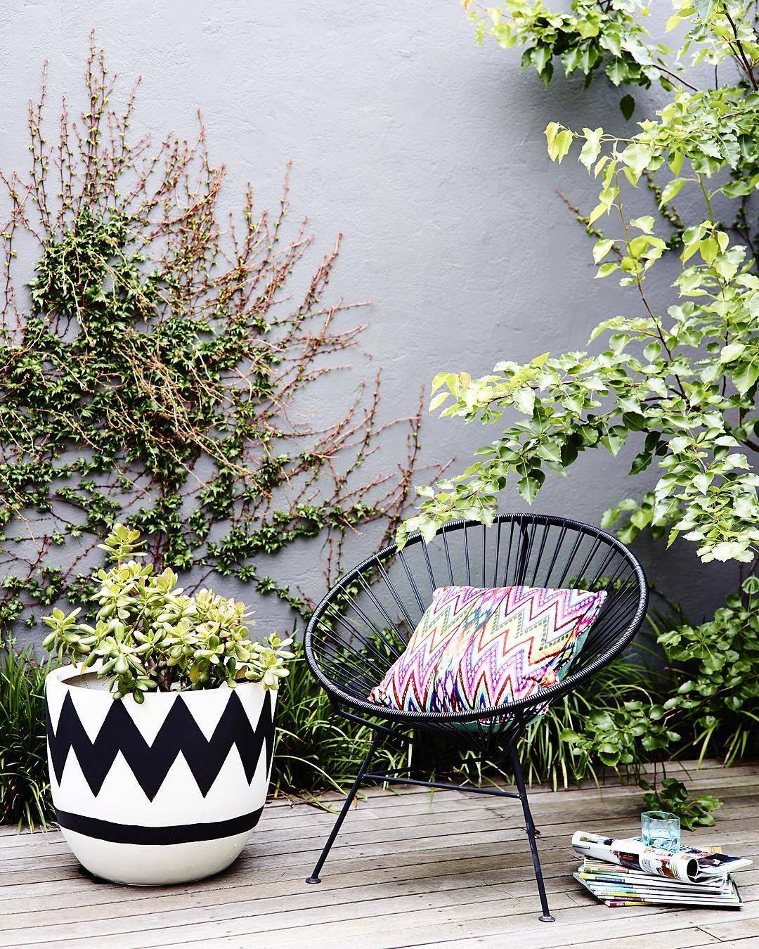 Terraza decorada con una silla Acapulco negra y un cojín de rayas zig zag