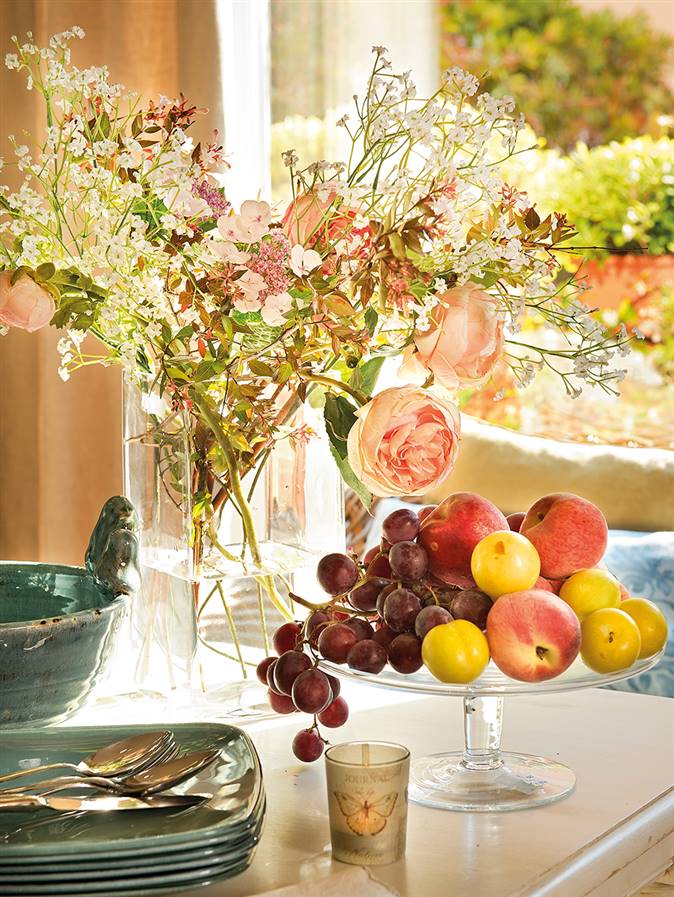 Detalle de vajilla, jarrón con flores y pastelero con fruta