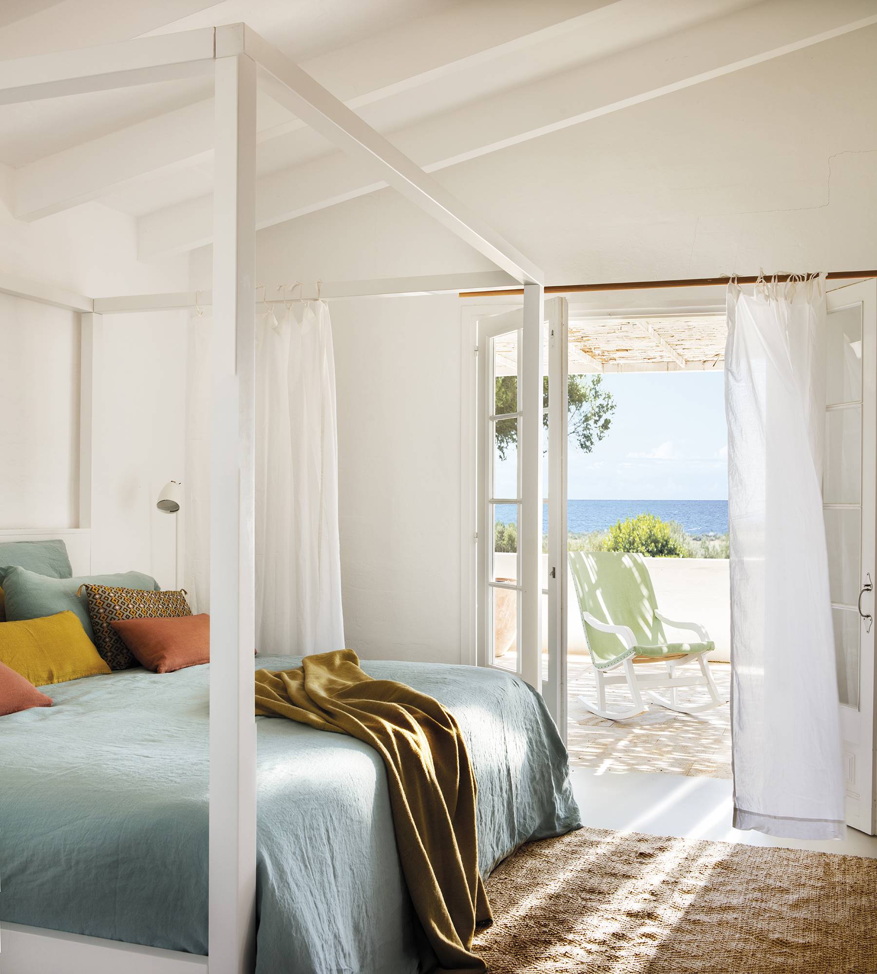 Dormitorio blanco con cama con dosel y terraza con vistas al mar