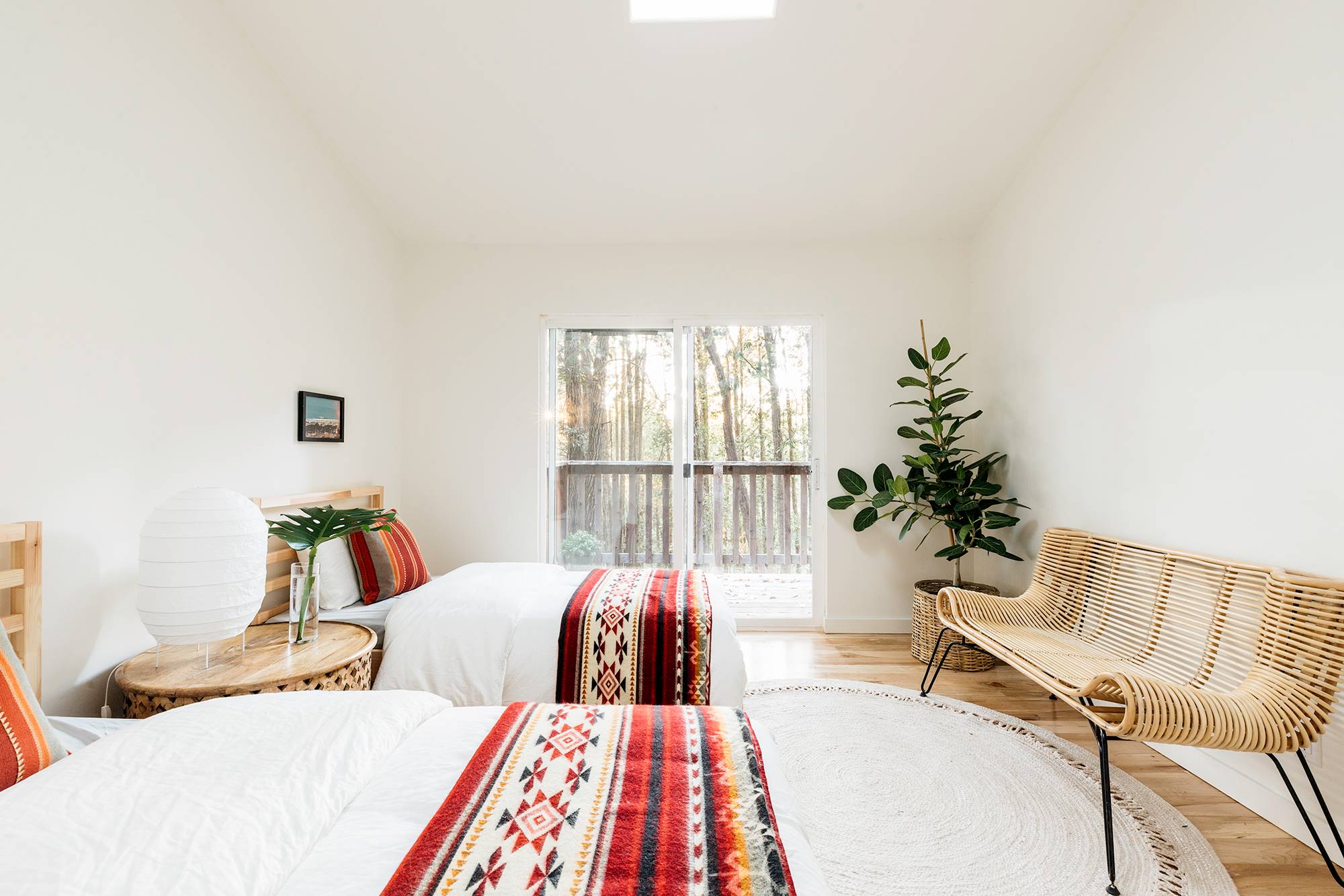 Dormitorio con dos camas de madera, ropa de cama étnica, un banco de madera y plantas