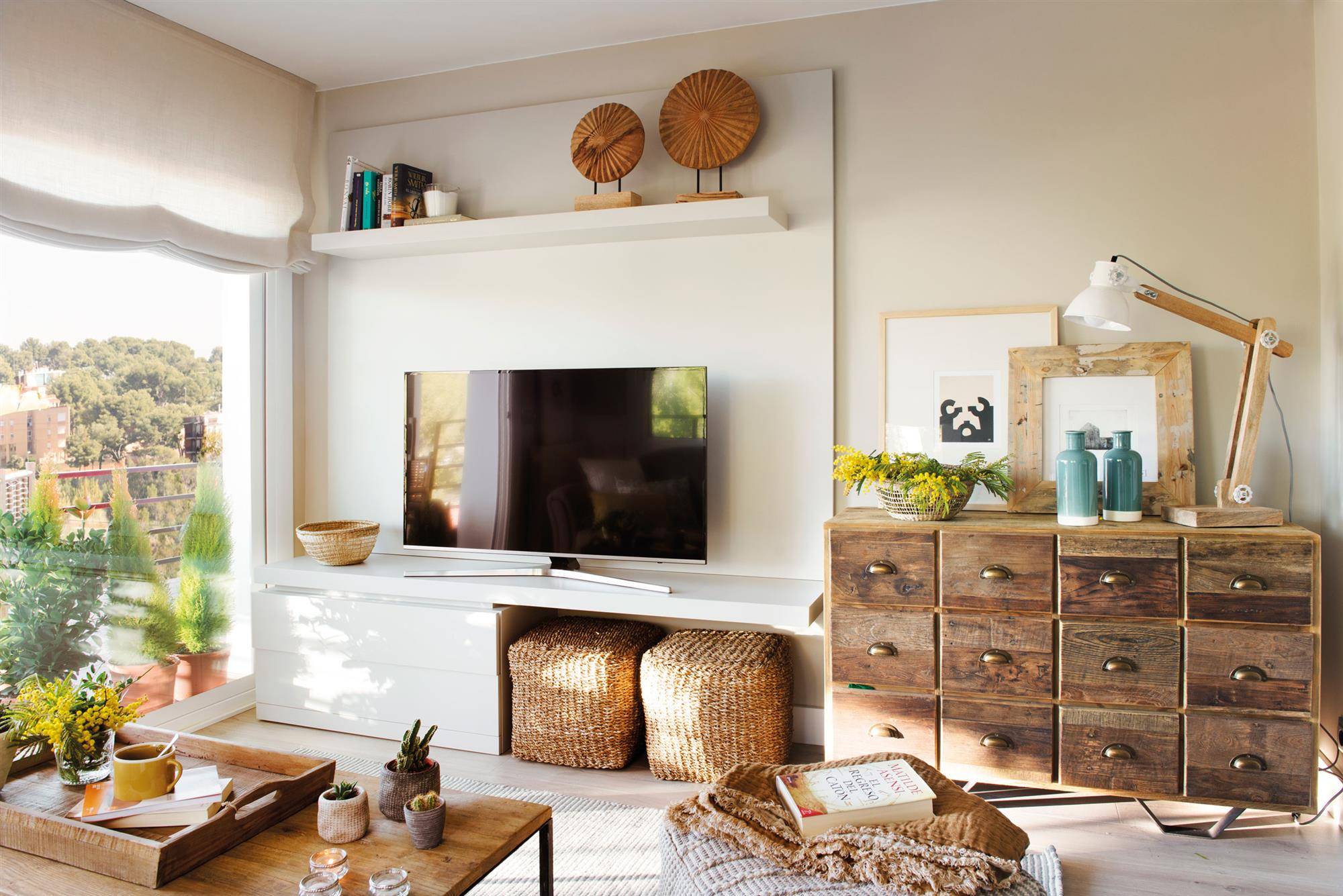 Salón con mueble de televisor blanco que alberga dos puffs y cómoda de madera con cajones. 