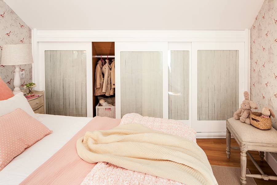 Dormitorio abuhardillado en tonos rosas y blancos con armario a medida. 