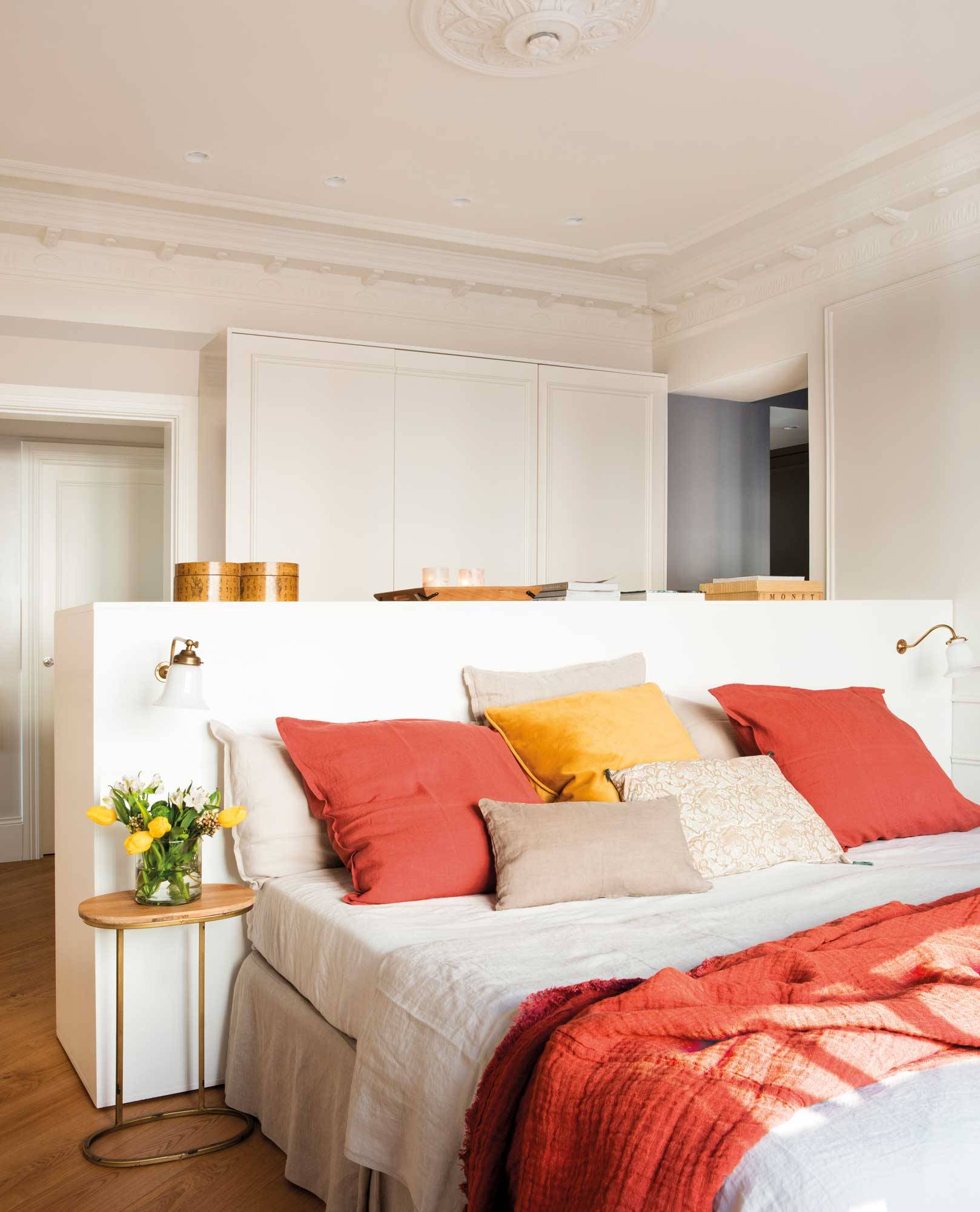 Dormitorio moderno con molduras clásicas y cabecero separando la zona de vestidor.