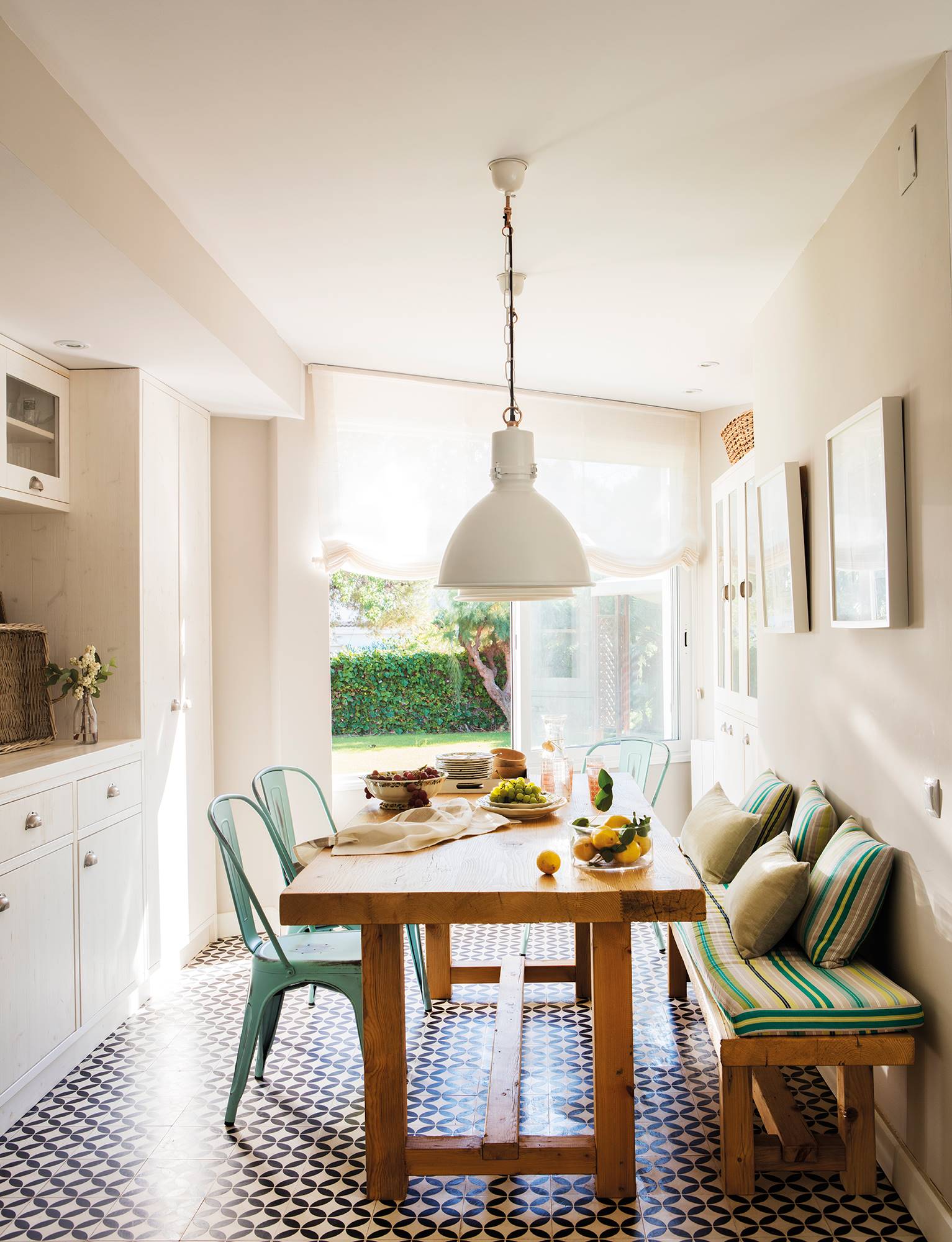 Office abierto a la cocina en blanco con mesa de madera y banco y sillas verdes.